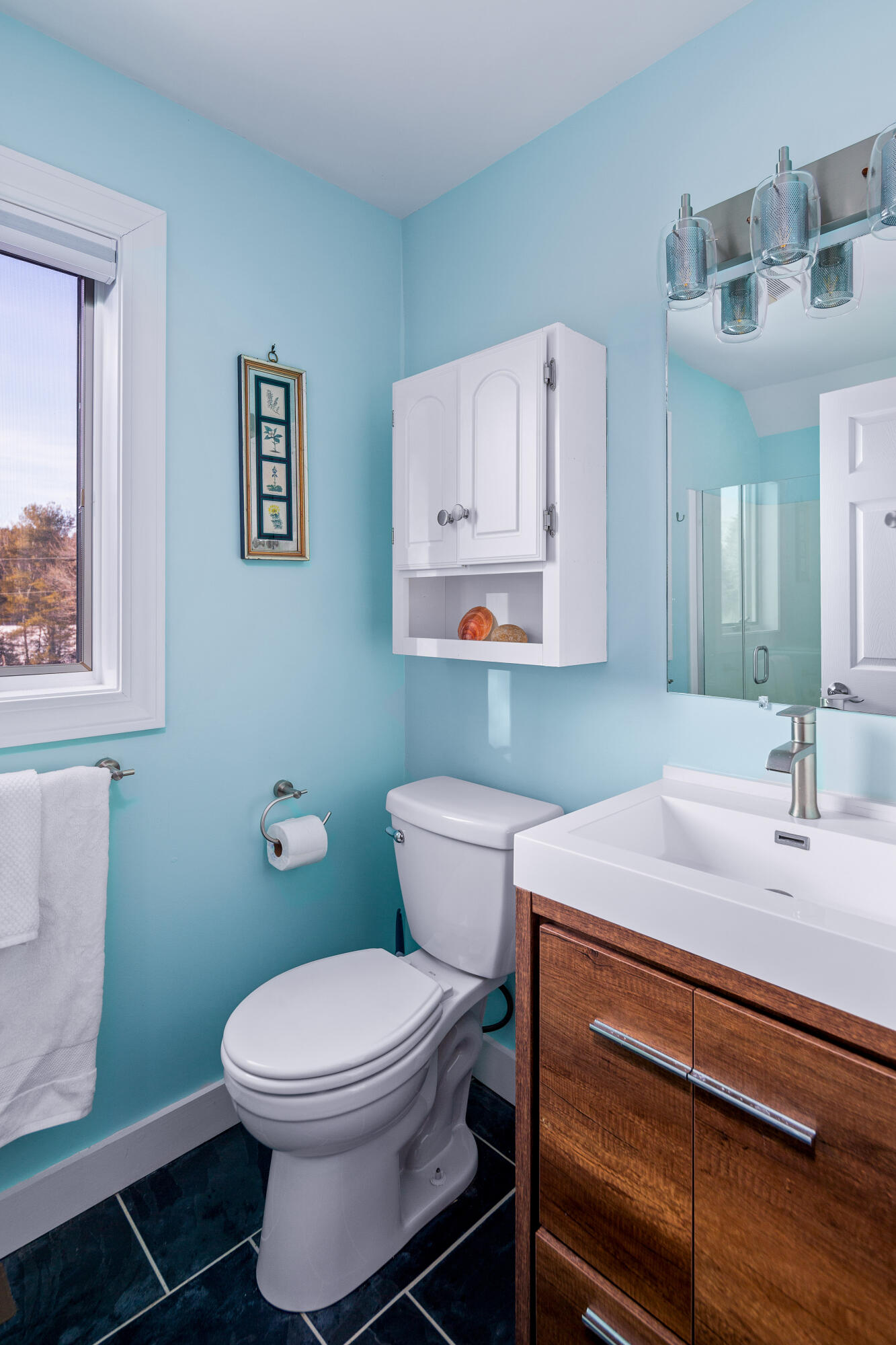 Bathroom with aqua walls, dark tile floor, and a wood vanity beside a white toilet.