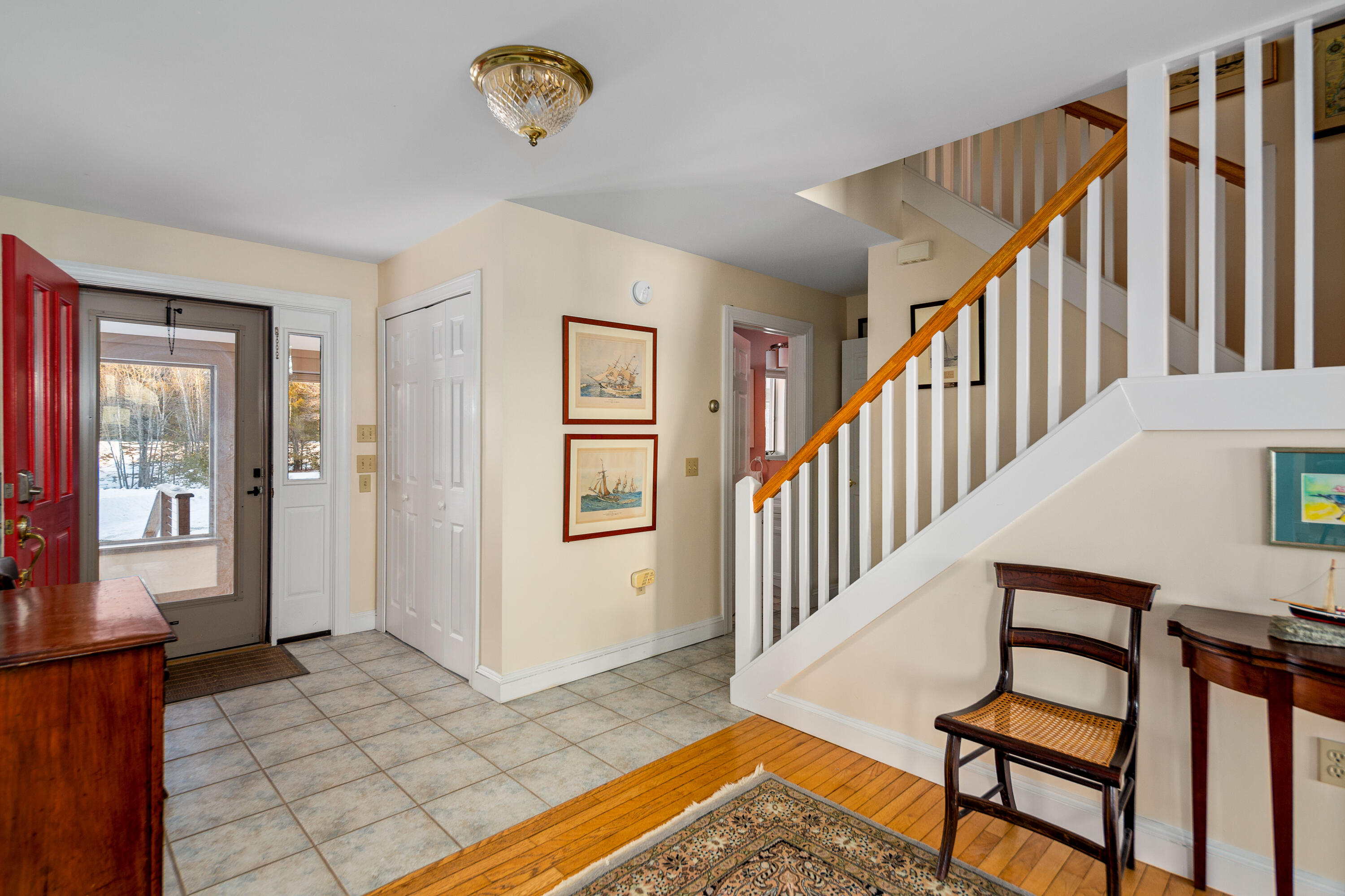 Home entryway with a red front door, tiled floor, and white staircase with a wooden handrail.