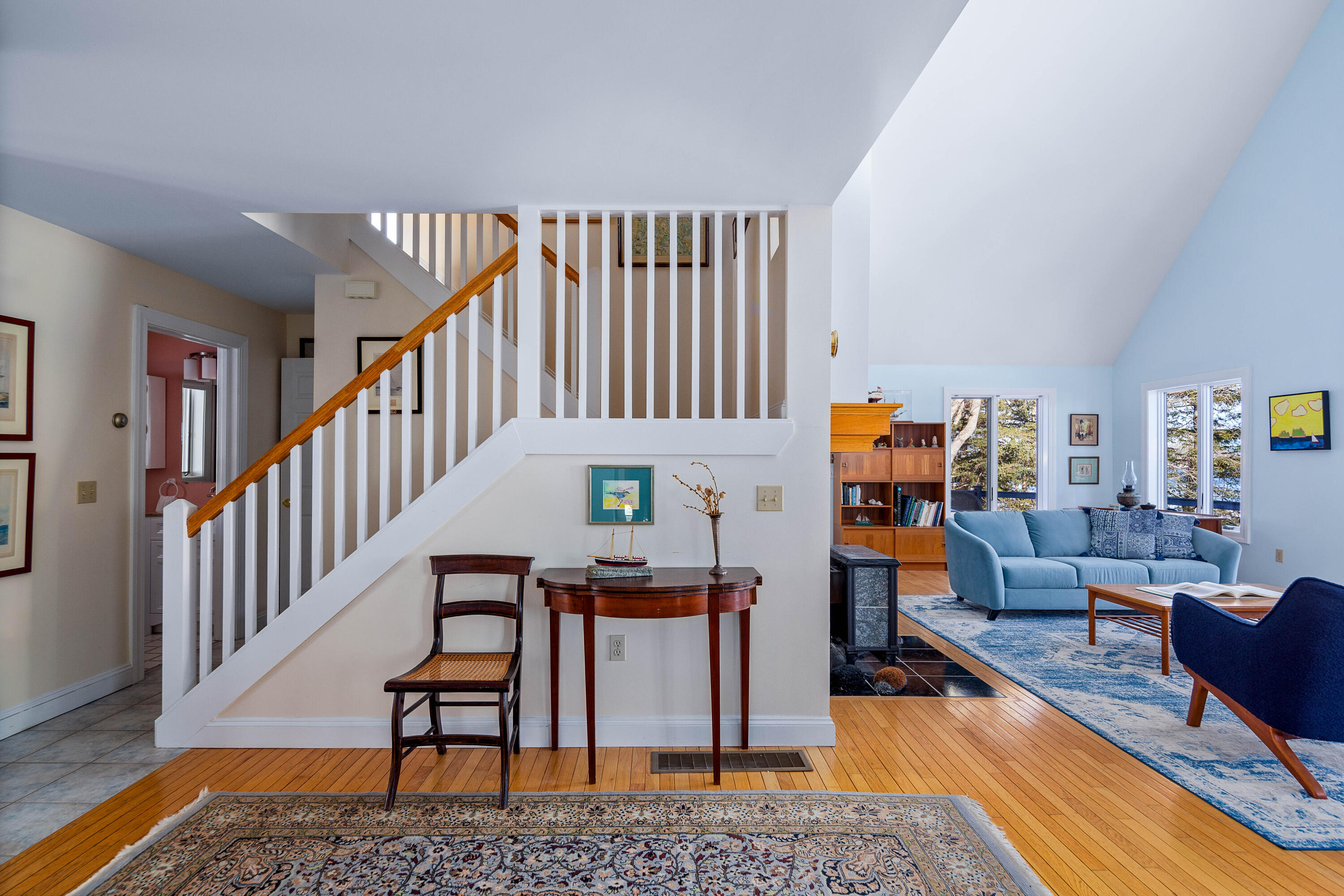 Furnished entry and living room with a white staircase, wood handrail, blue sofa, and hardwood floors.