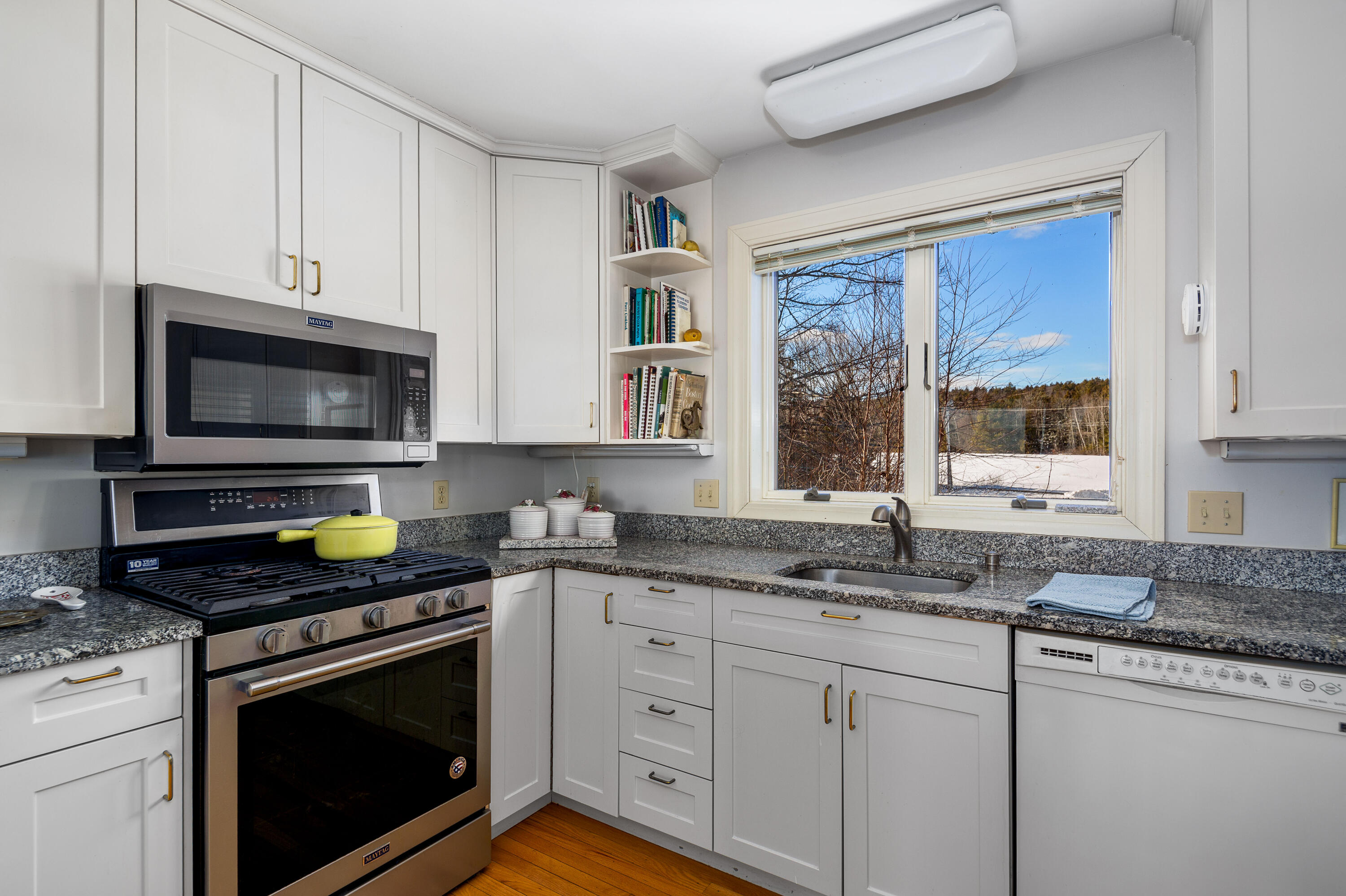 Kitchen with white cabinets, granite counters, stainless appliances, and a window overlooking snowy woods.