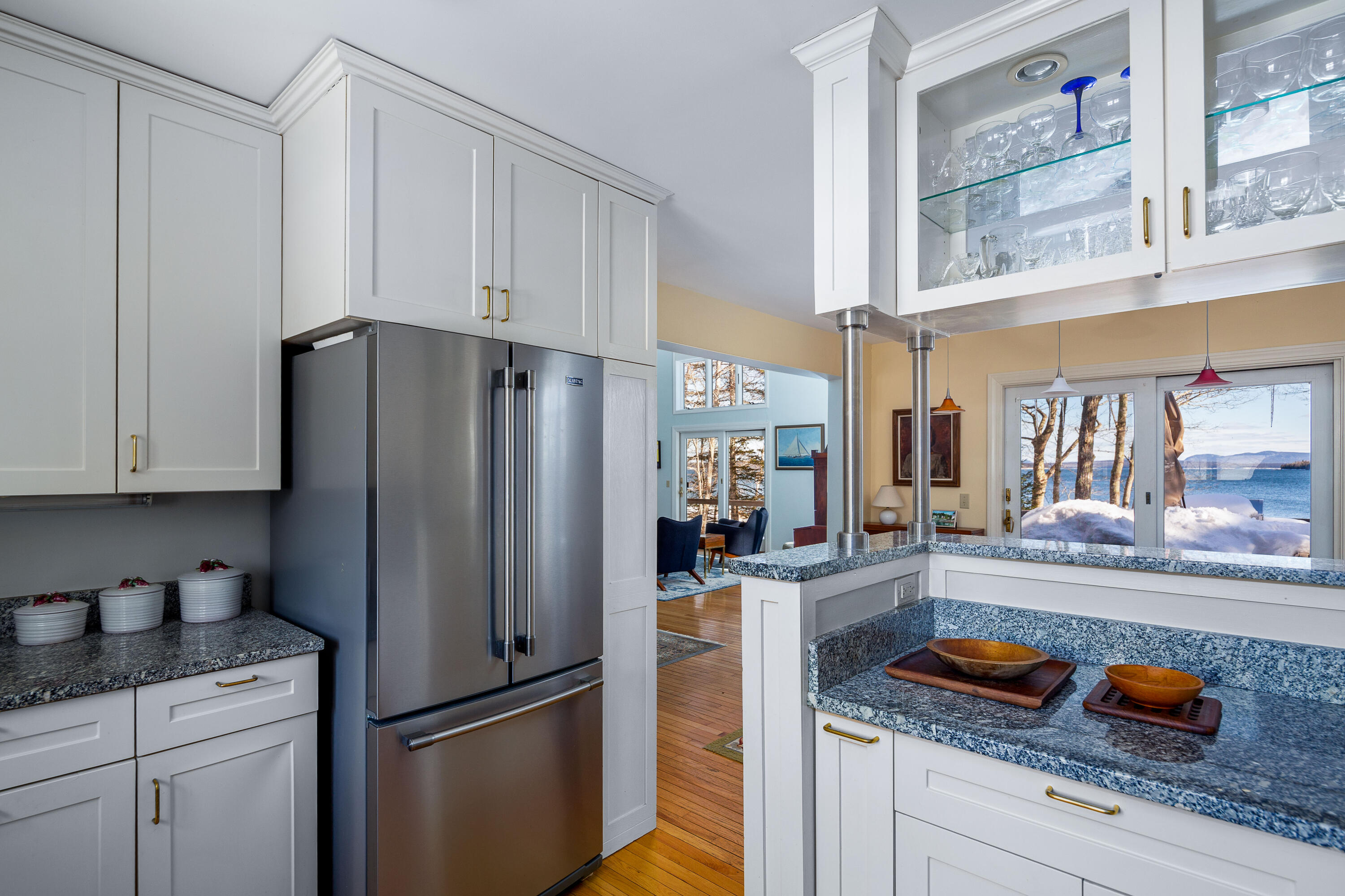 White kitchen with granite counters and stainless refrigerator, overlooking snowy shoreline and water.