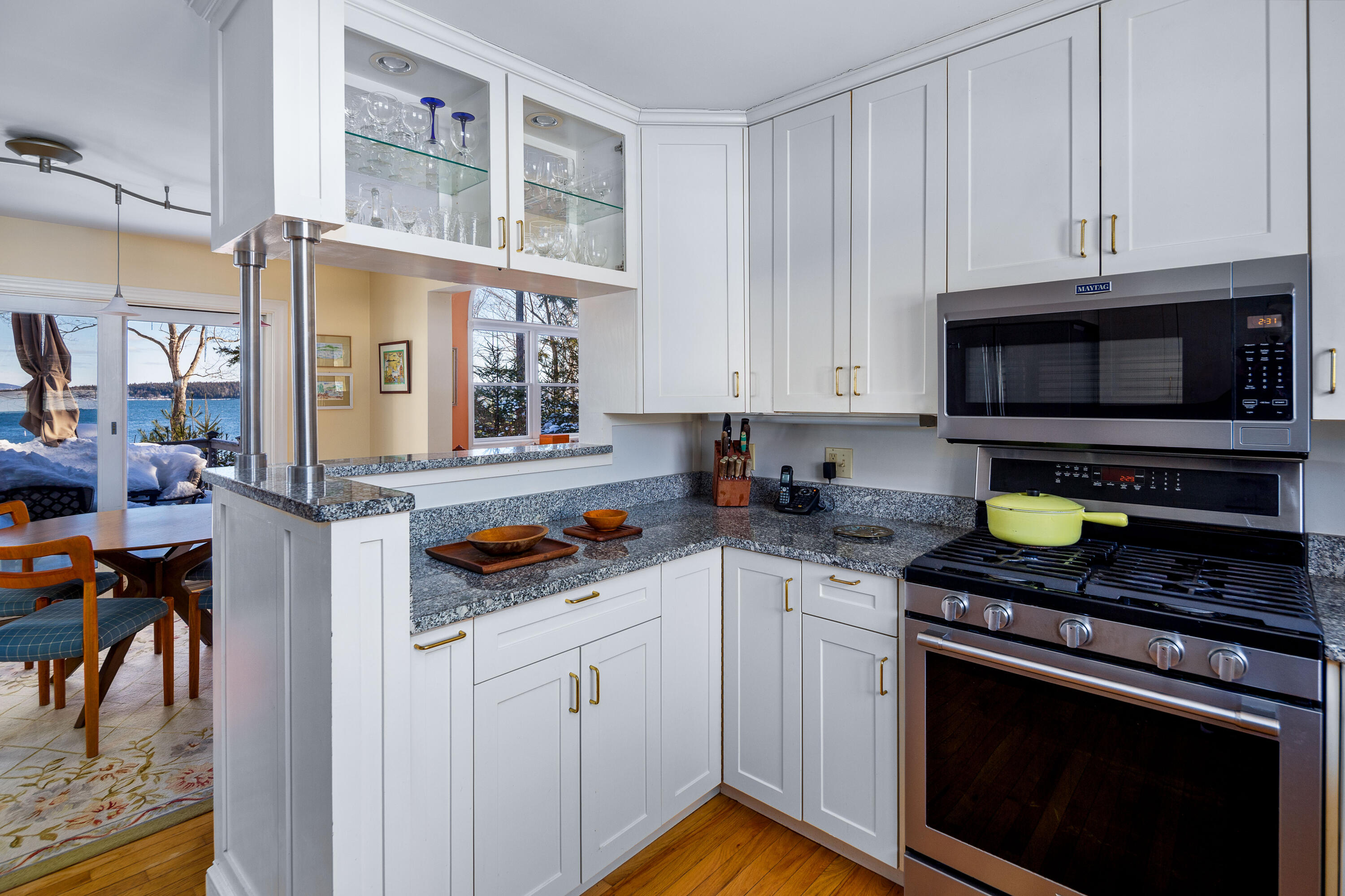Kitchen with white cabinets, granite counters, stainless range, and windows overlooking a snowy waterfront.