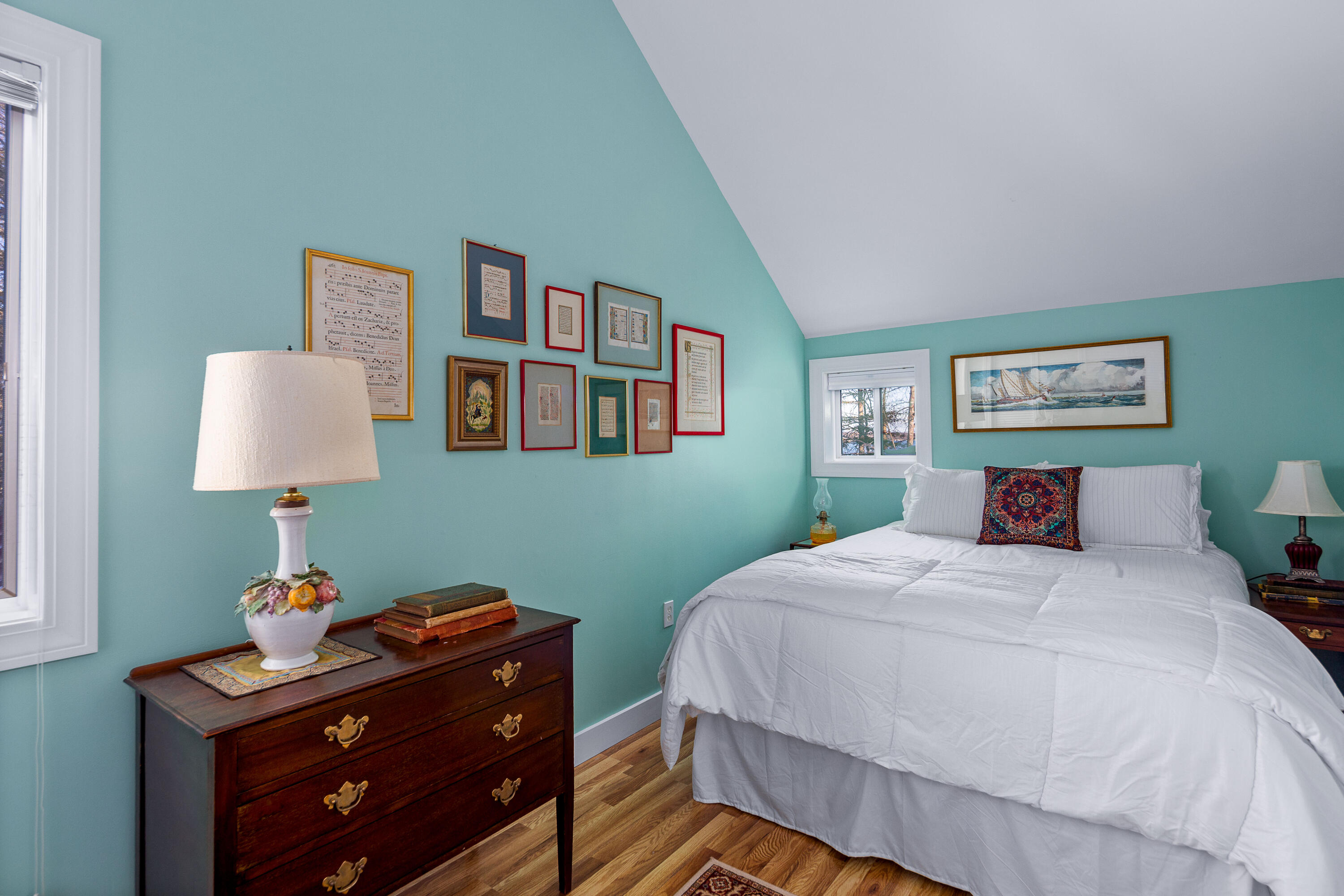 Bedroom with aqua walls, a white bed, framed artwork, and a dark wooden dresser topped with a lamp.