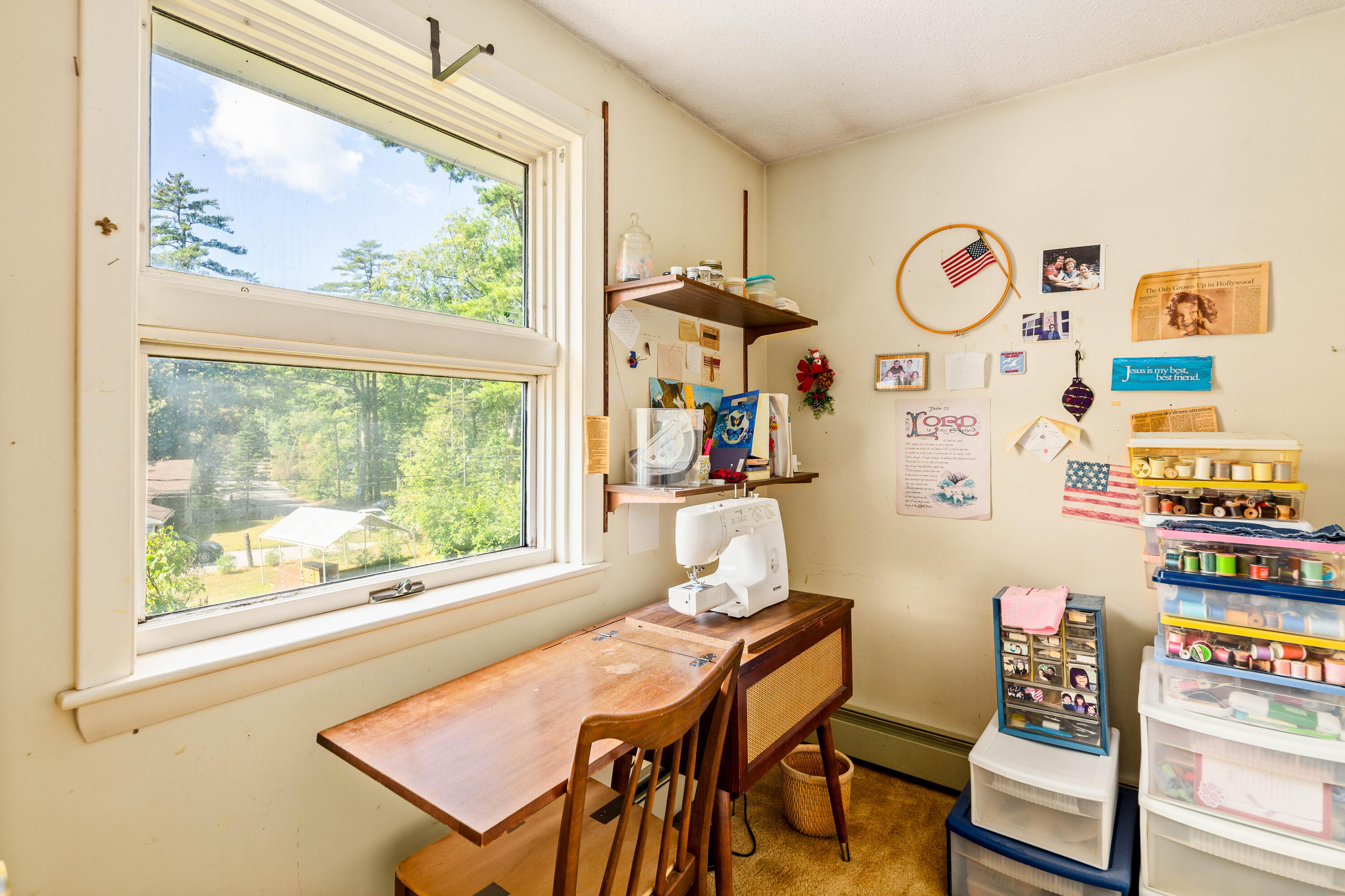 Craft room with sewing machine, wooden worktable, and a large window overlooking trees.