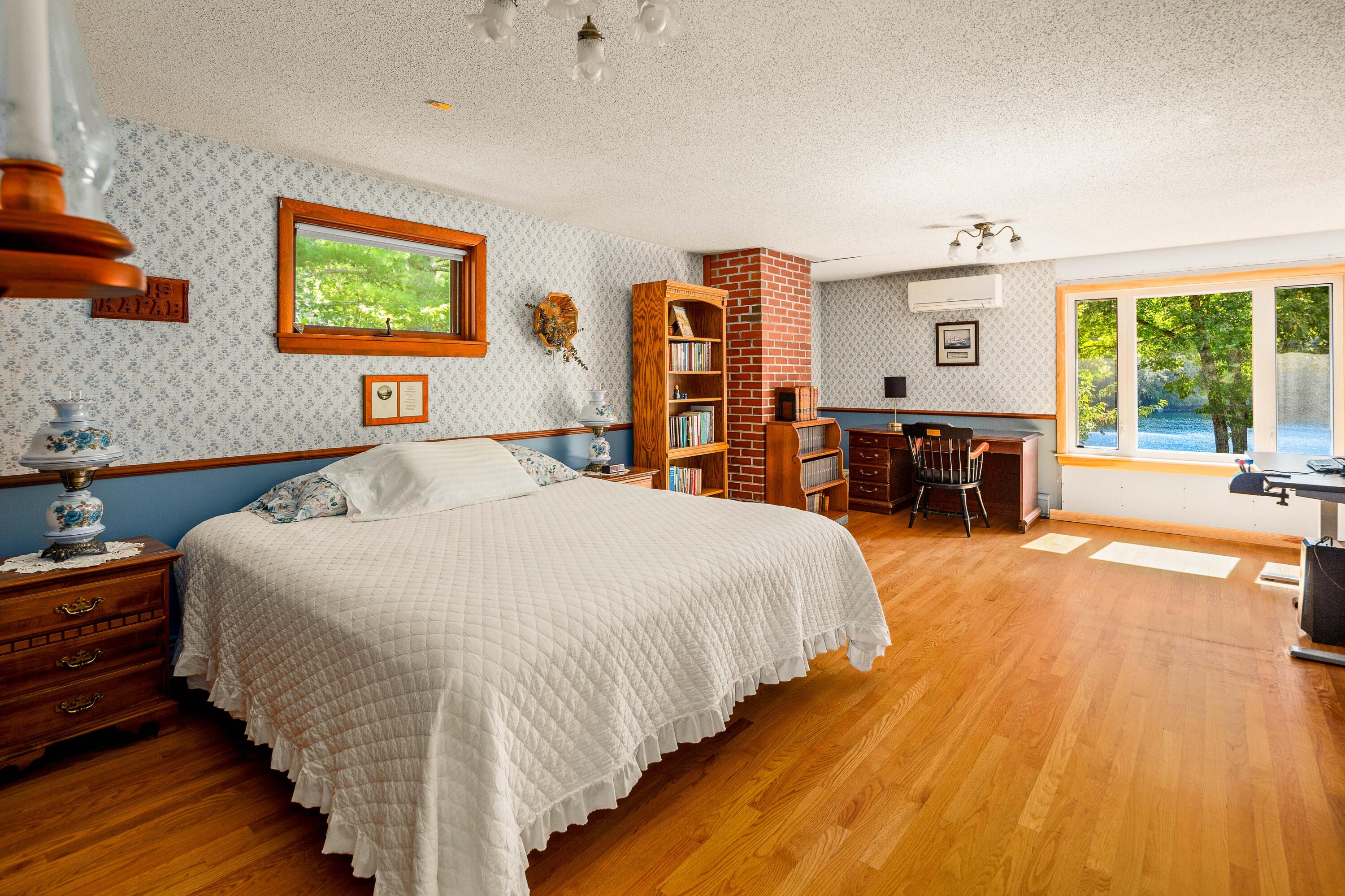Furnished bedroom with hardwood floors, a brick column, and windows overlooking the water.