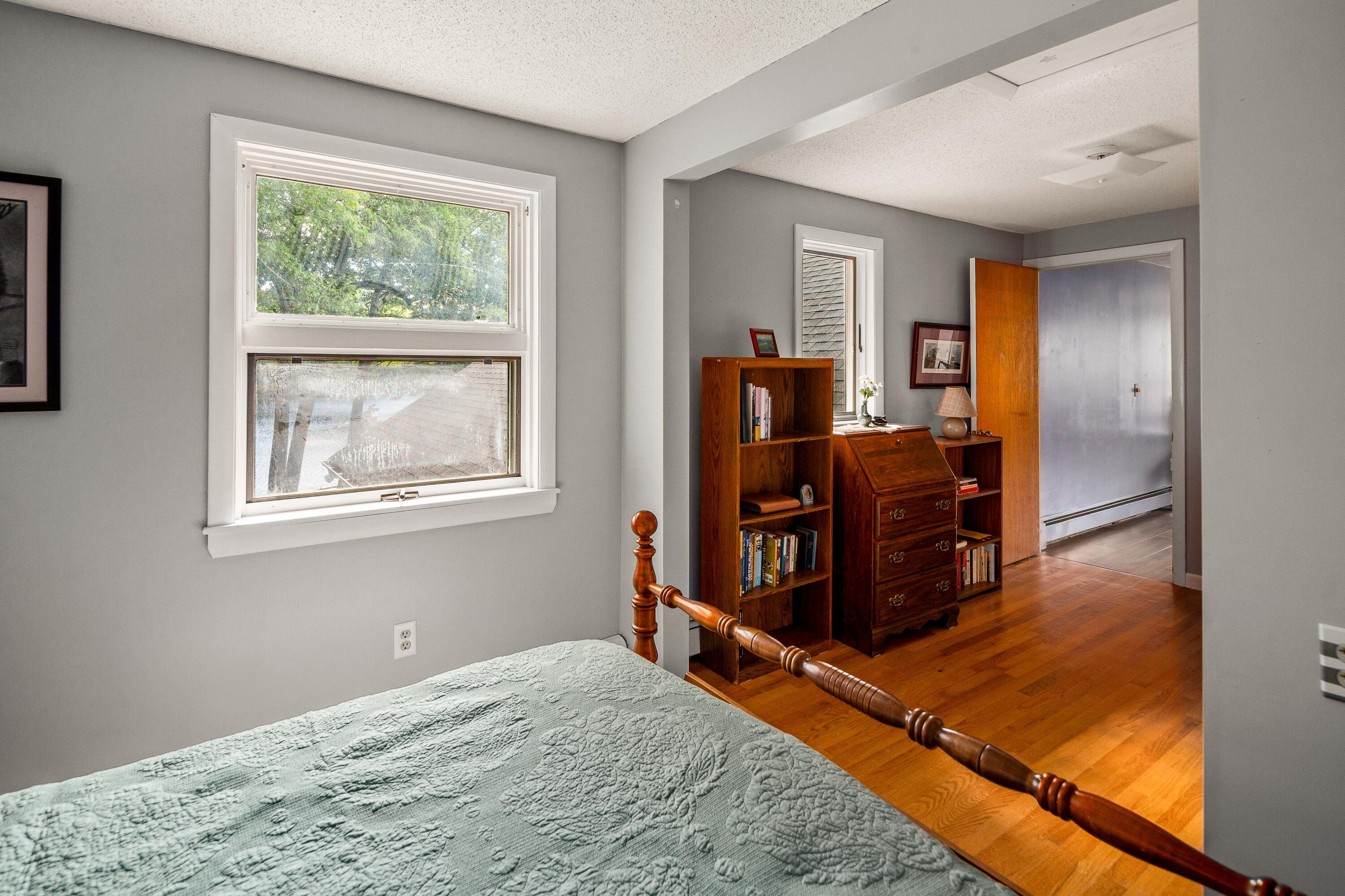 Bedroom with a carved wooden bed, hardwood floors, and a window overlooking trees.