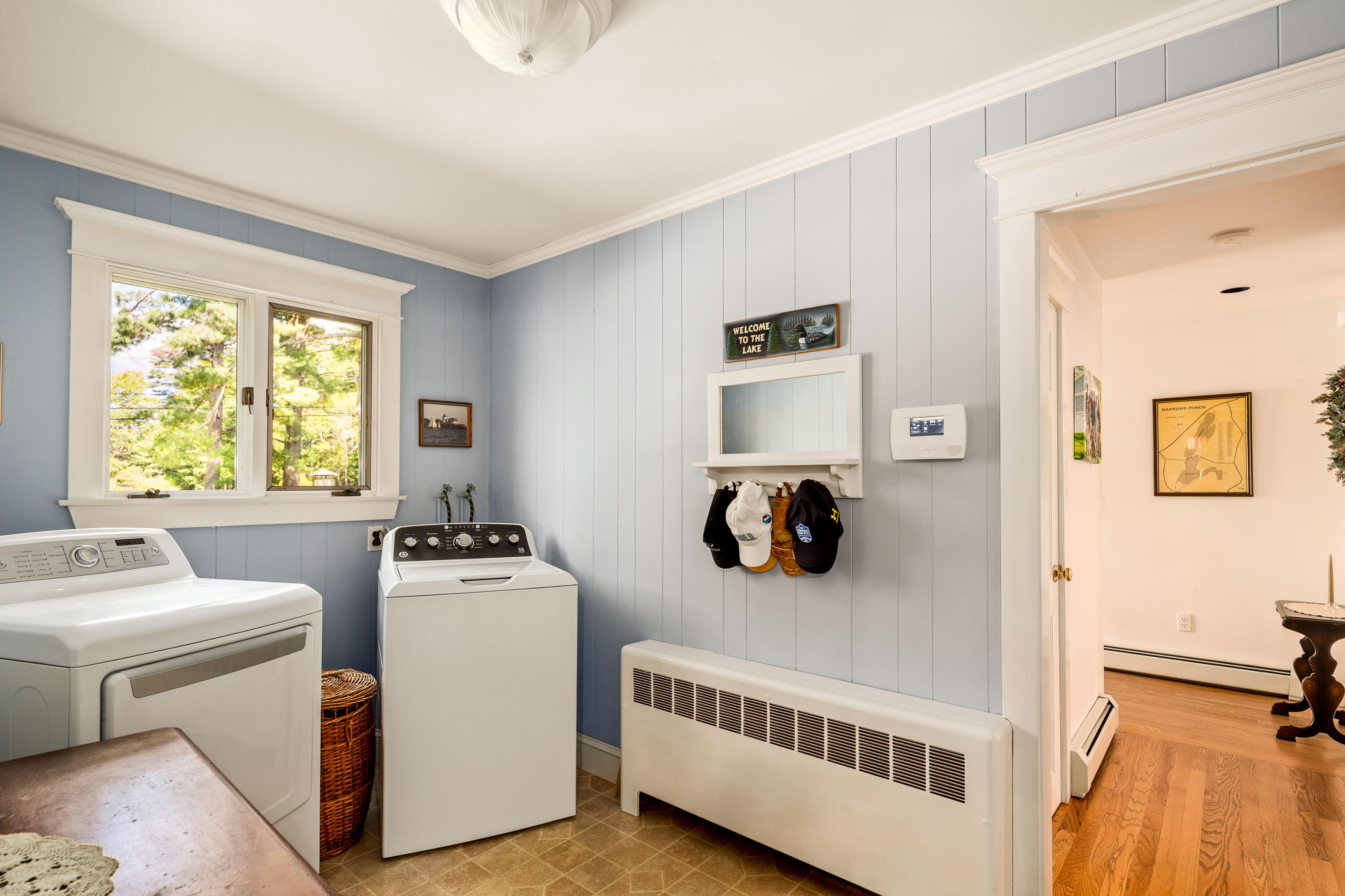 Laundry room with blue paneled walls, washer and dryer, and a window overlooking trees.
