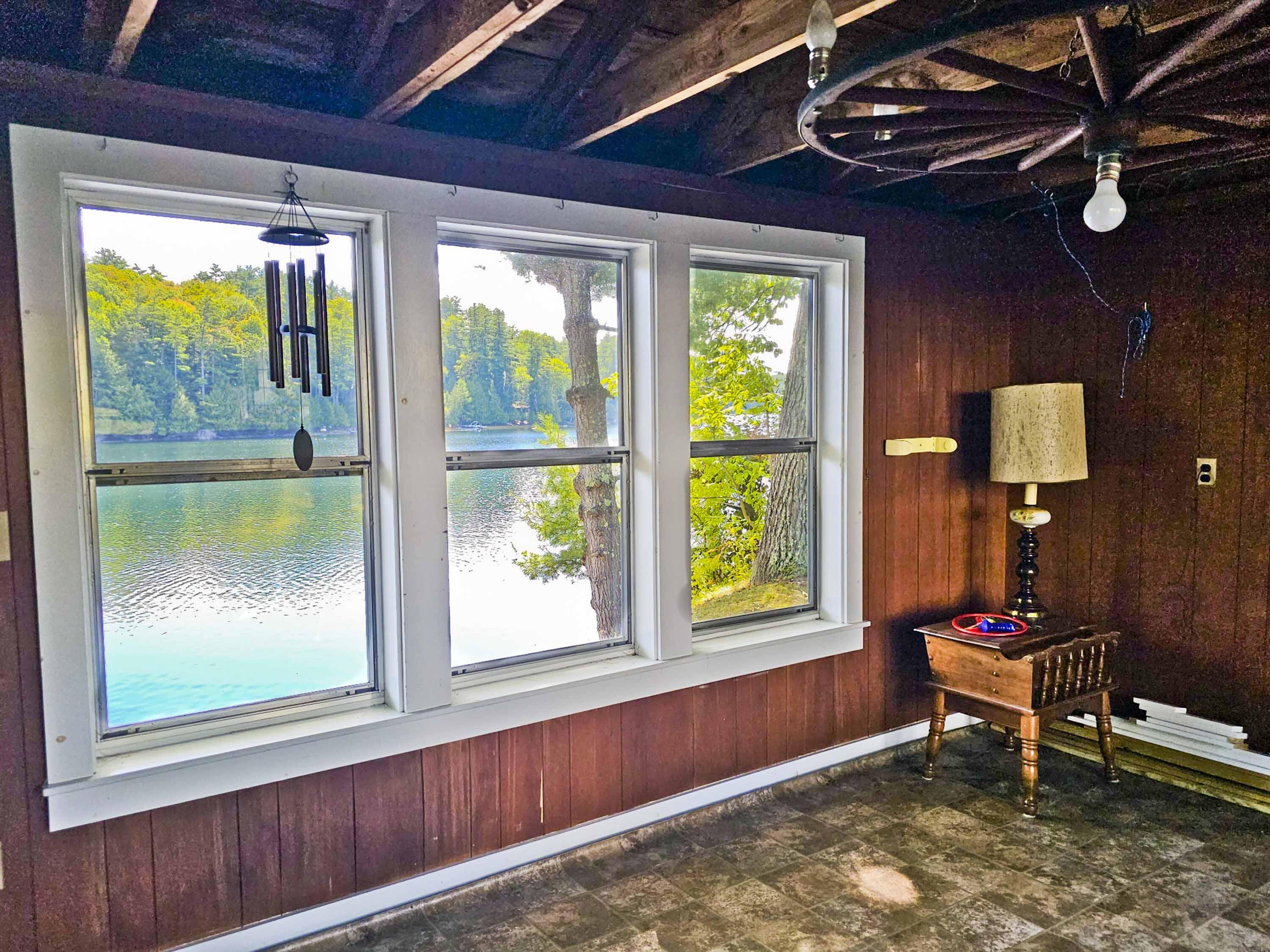 Room with three windows overlooking a lake, wood-paneled walls, and exposed ceiling beams.