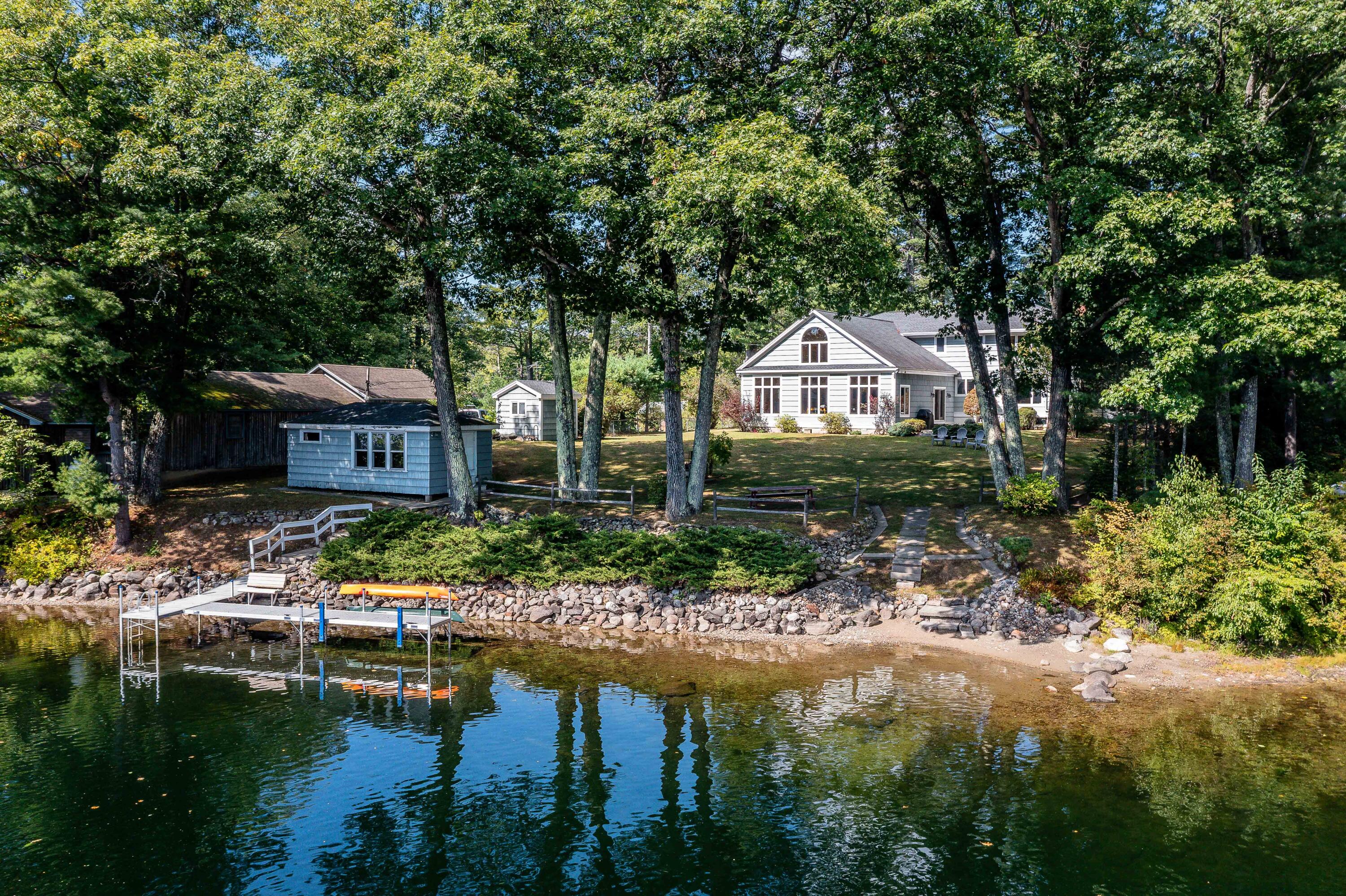 Lakeside home among trees, with a small dock and kayak along the rocky shore.