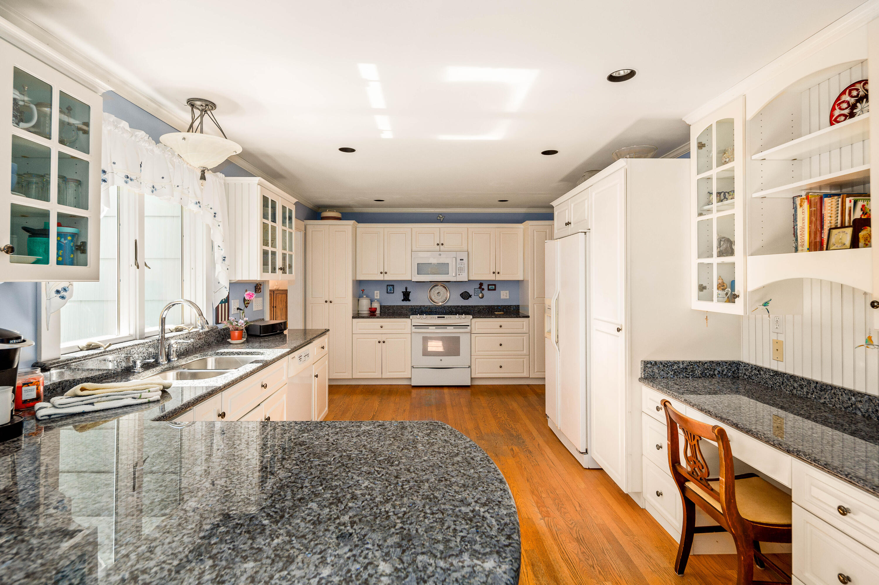 Kitchen with white cabinetry, granite counters, a central island, and hardwood floors.