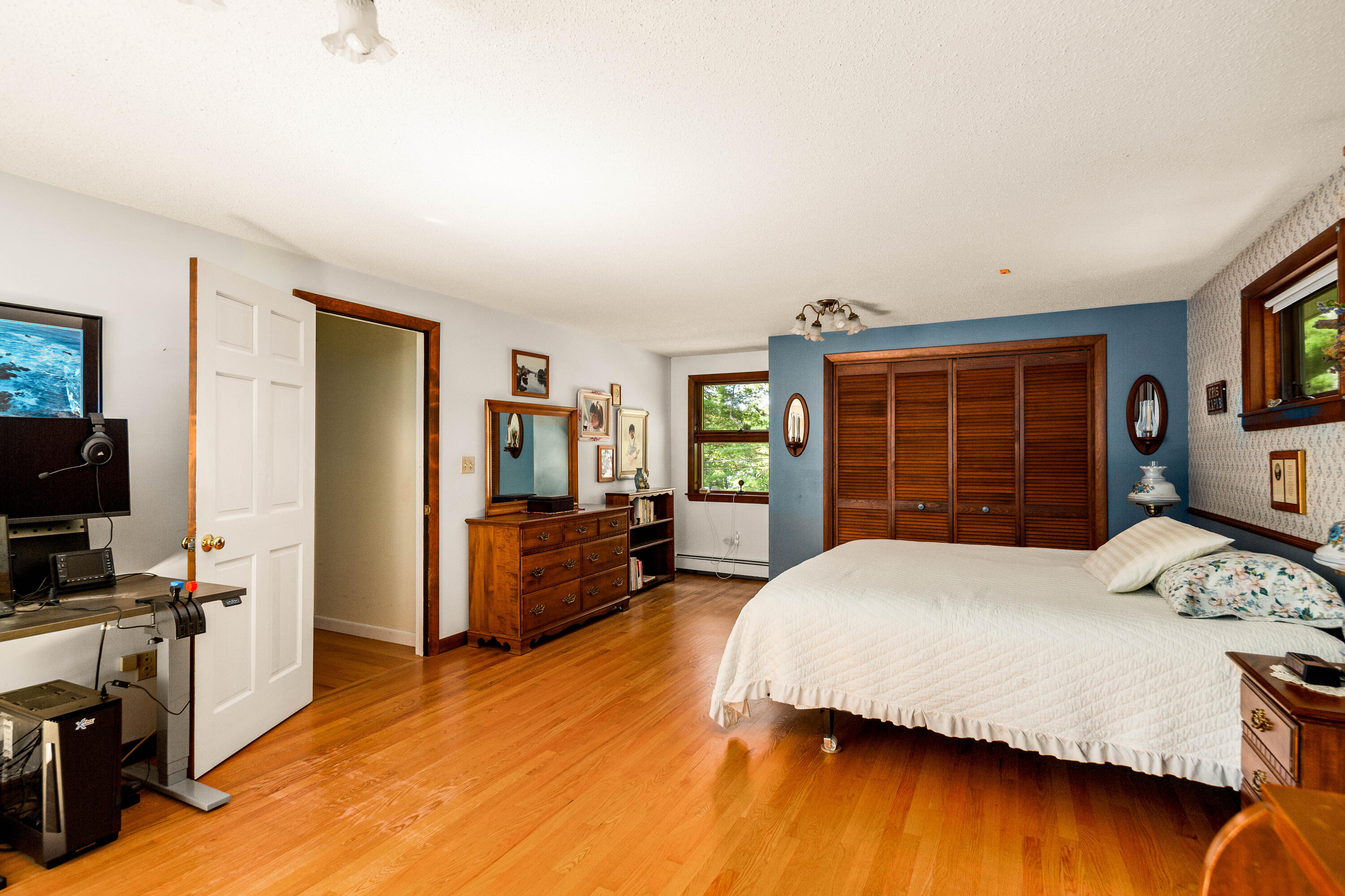 Bedroom with hardwood floors, blue accent wall, and a large bed beneath wood louvered closet doors.