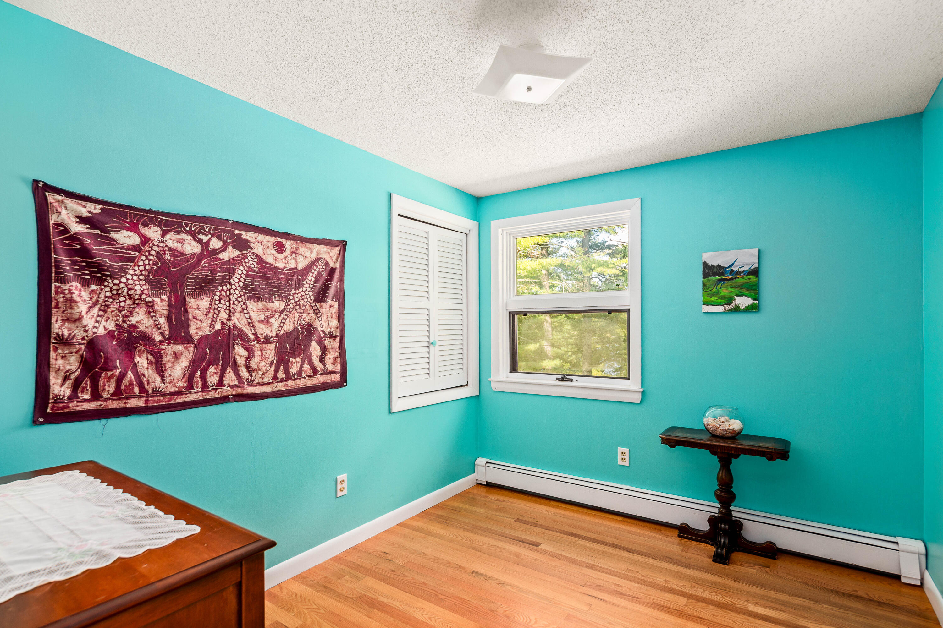 Bedroom with turquoise walls, hardwood floors, a window, and an elephant tapestry.