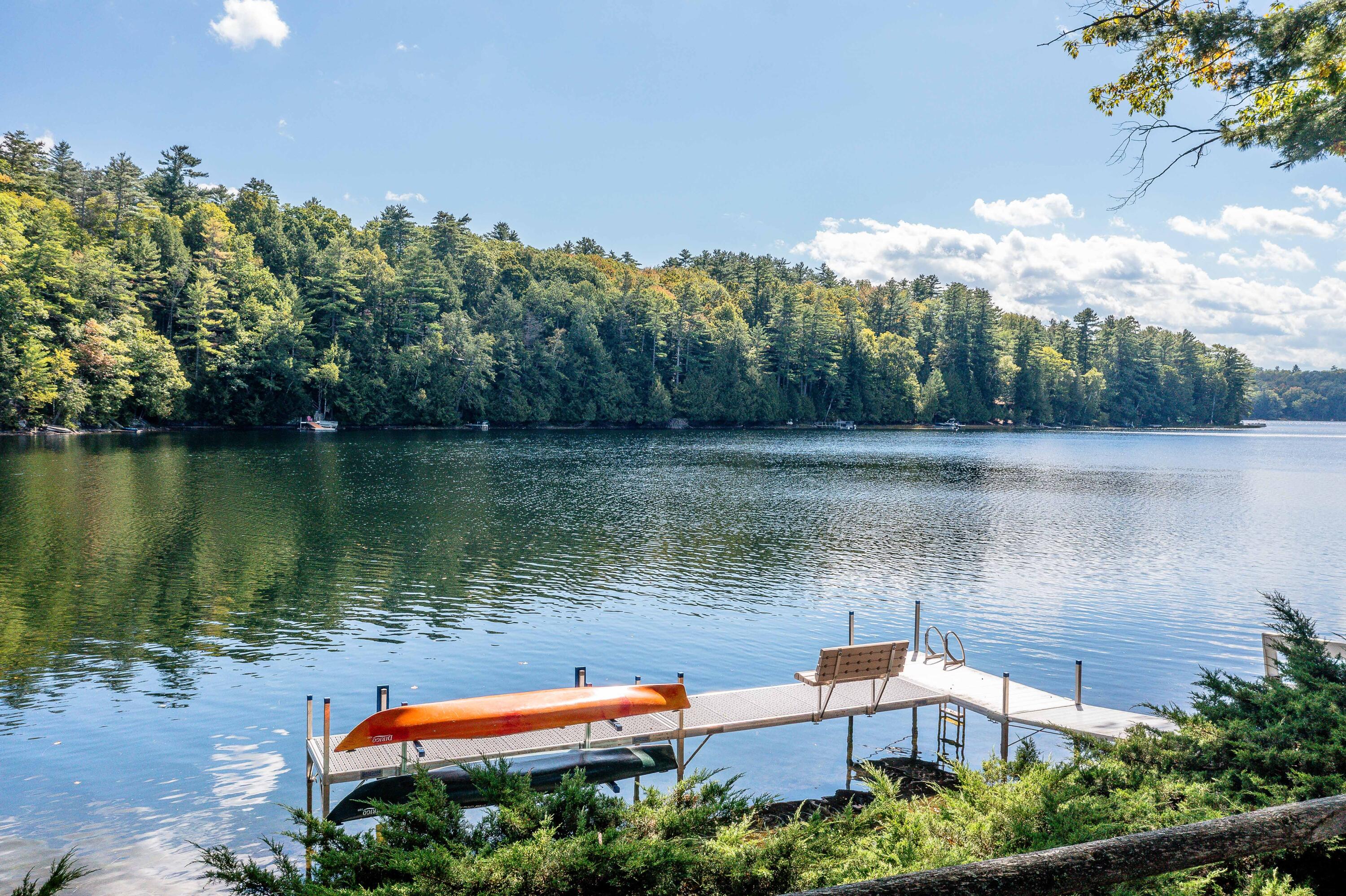 Dock with kayaks and a bench extending into a calm lake below a wooded shoreline.