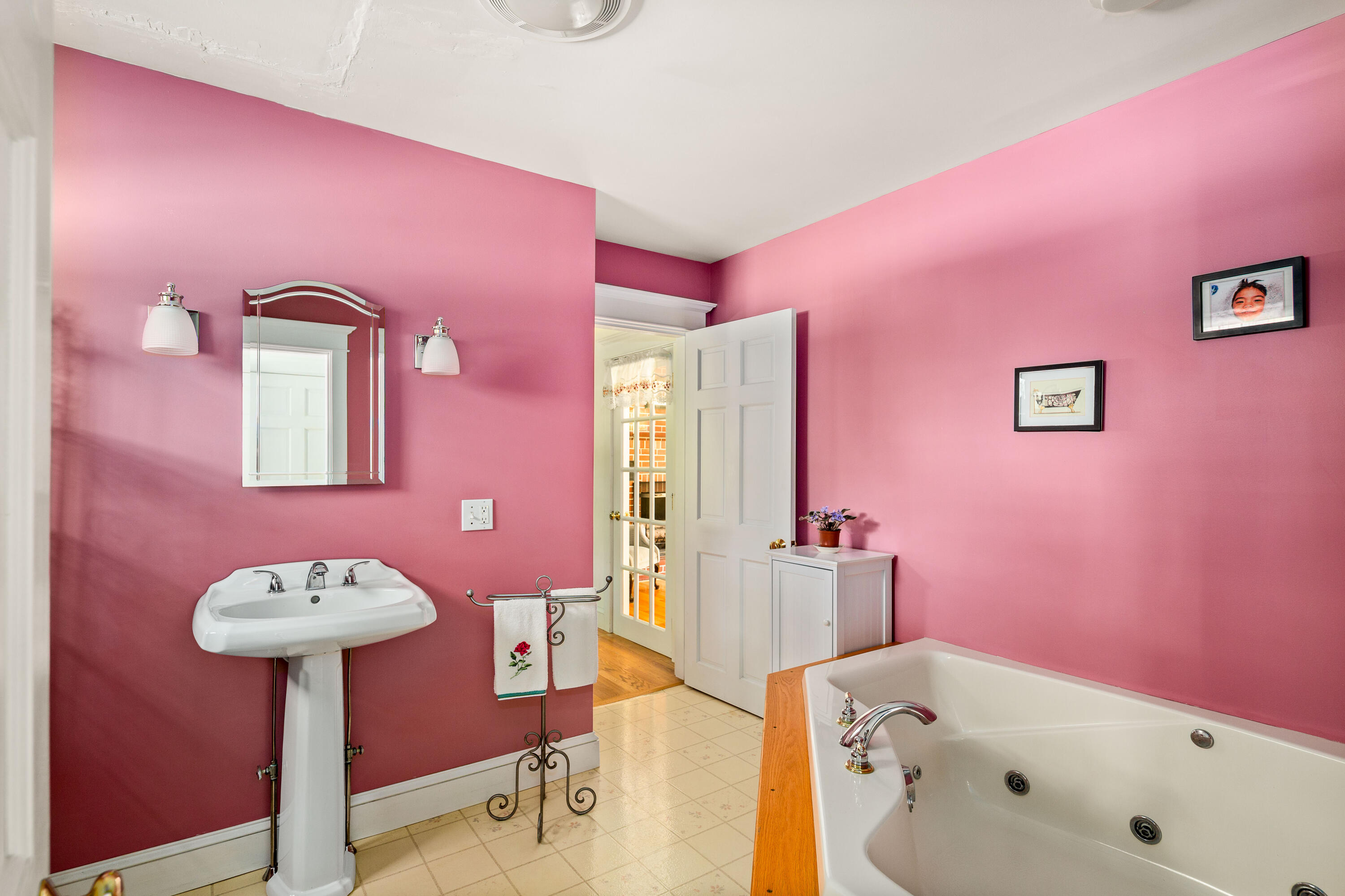 Bathroom with pink walls, a pedestal sink, and a built-in jetted tub with wood trim.