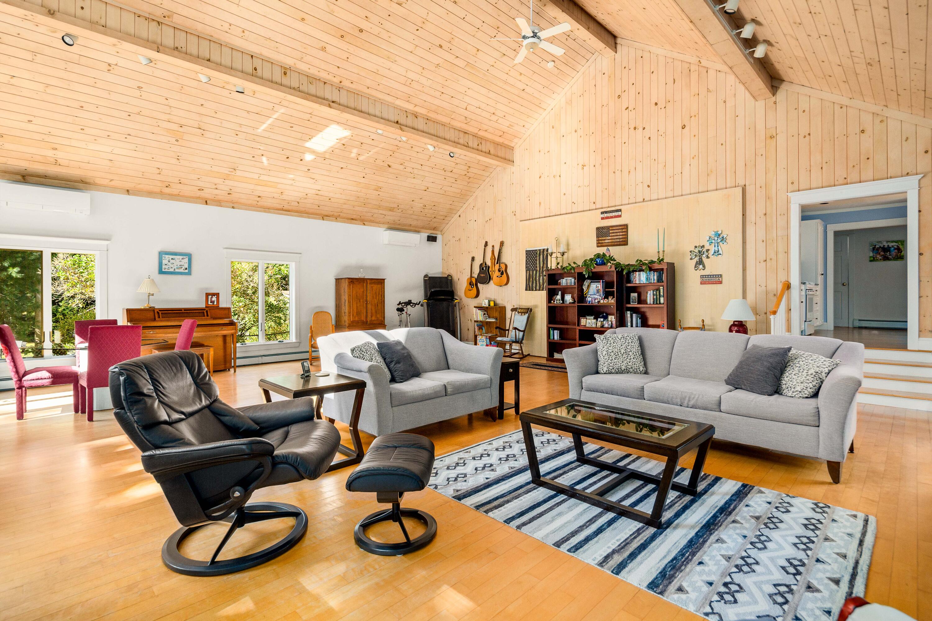 Furnished living room with a vaulted wood ceiling, gray sofas, and a piano by the windows.