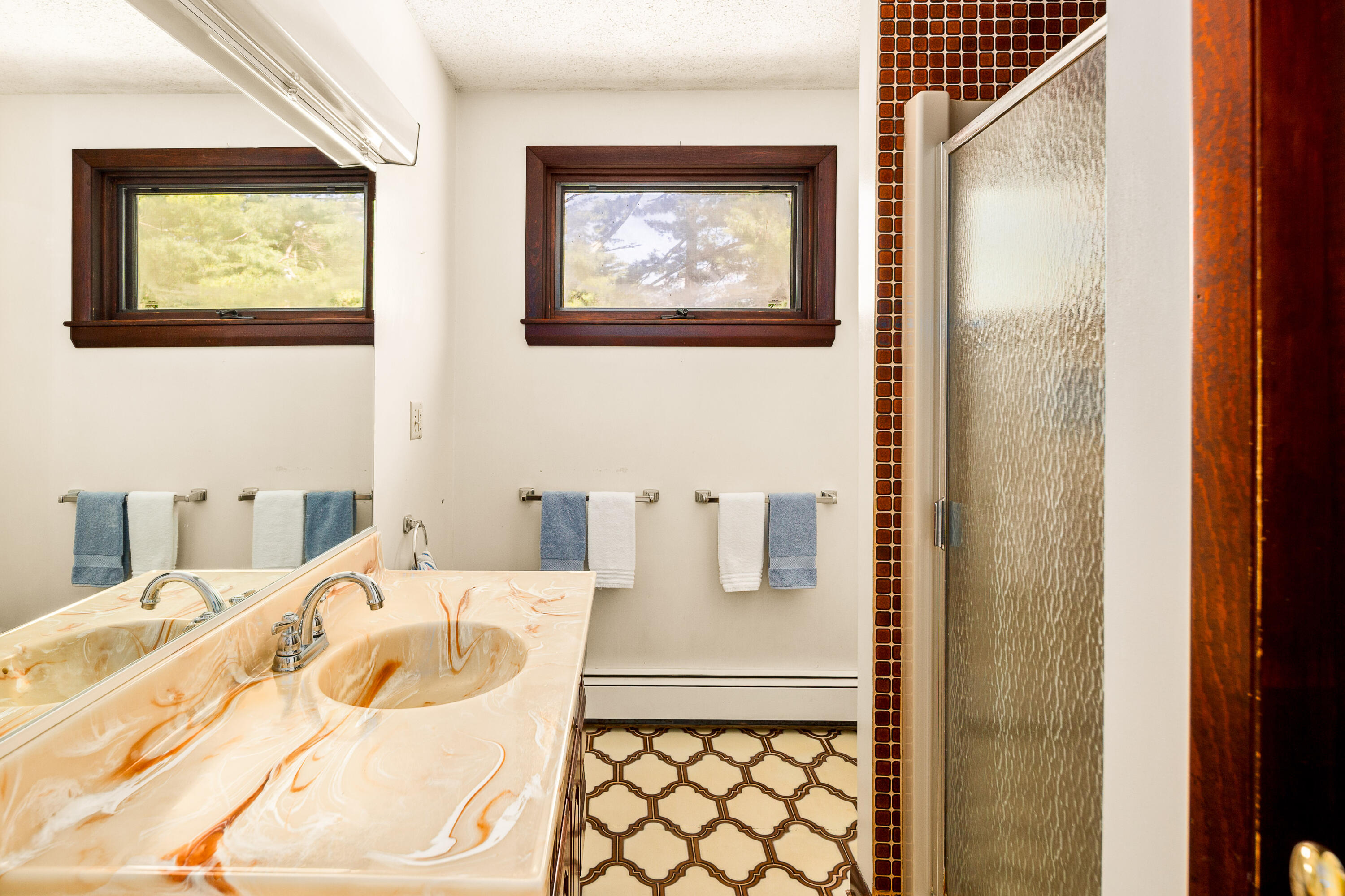 Bathroom with a marble-pattern double vanity, patterned floor tile, and a glass-enclosed shower.