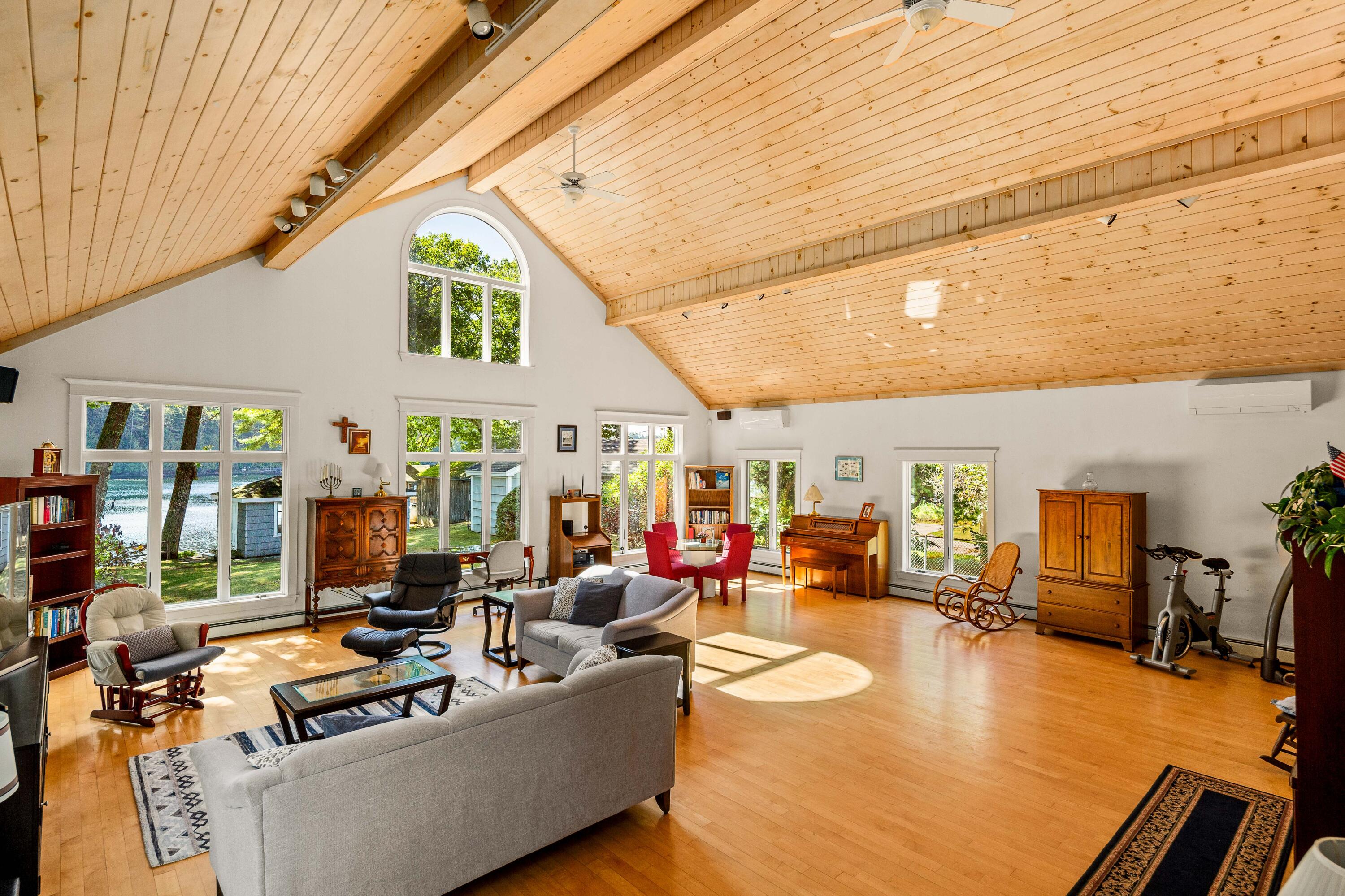 Furnished living room with a vaulted wood ceiling, expansive windows, and water visible outside.