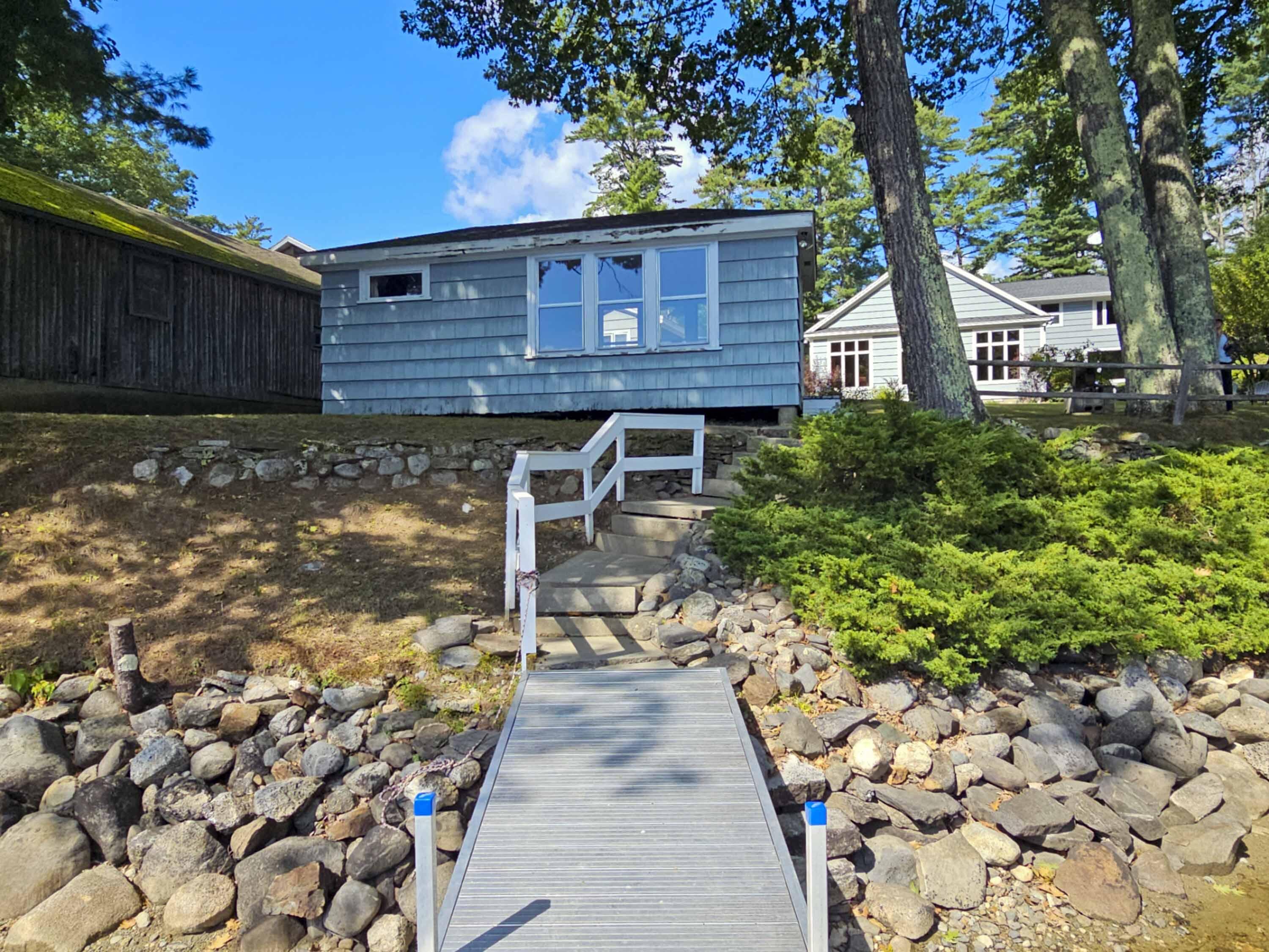 Blue lakeside cottage above a rocky shore, with a walkway leading to its entrance.