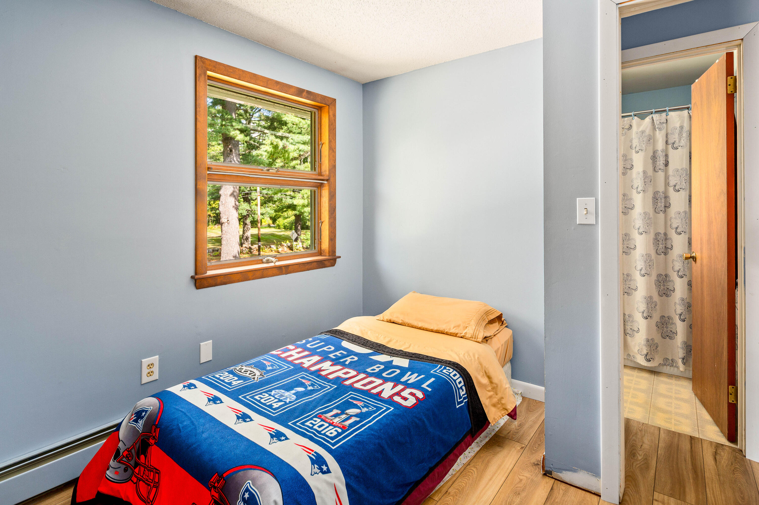 Bedroom with a New England Patriots Super Bowl blanket, wood-trimmed window, and adjoining bathroom.