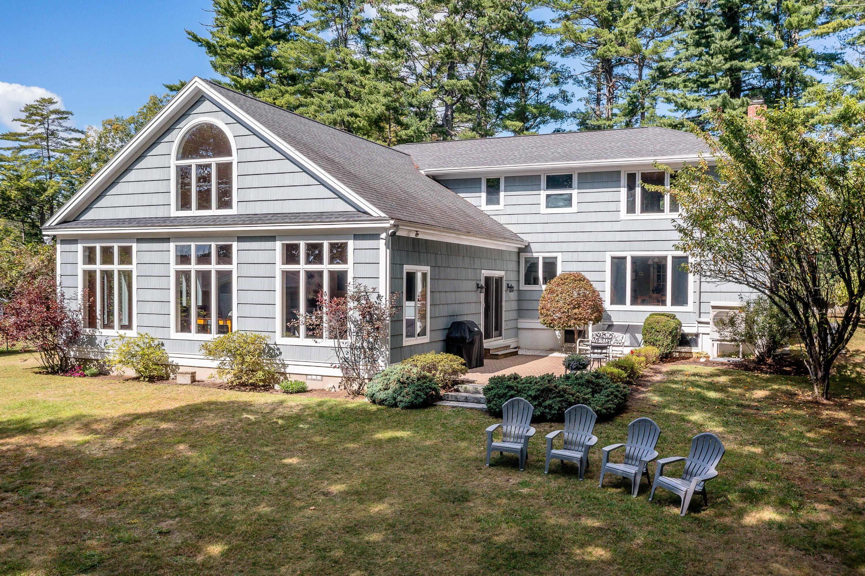 Gray shingle-sided home with a distinctive arched window and Adirondack chairs on the lawn.