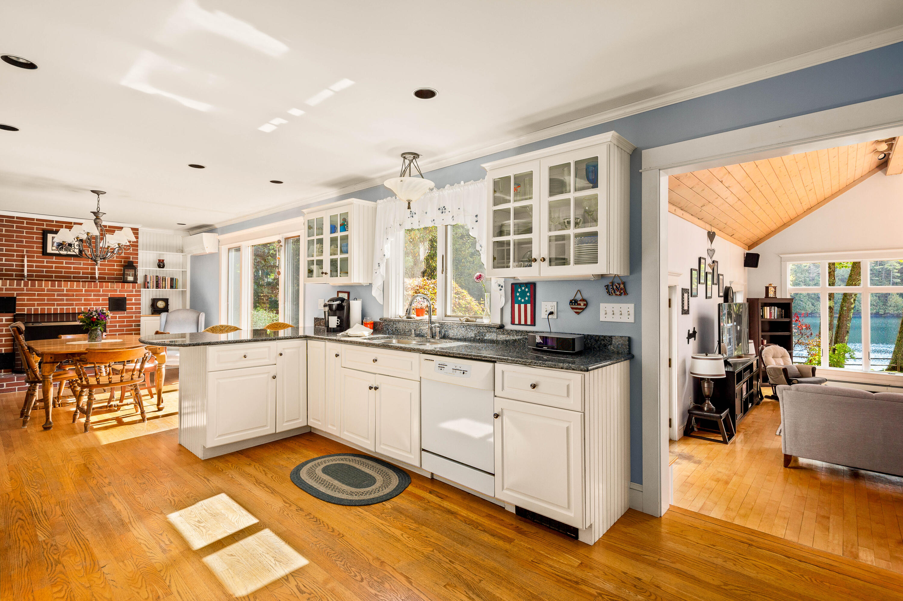 Bright kitchen with white cabinets and granite counters, opening to a living room overlooking the water.