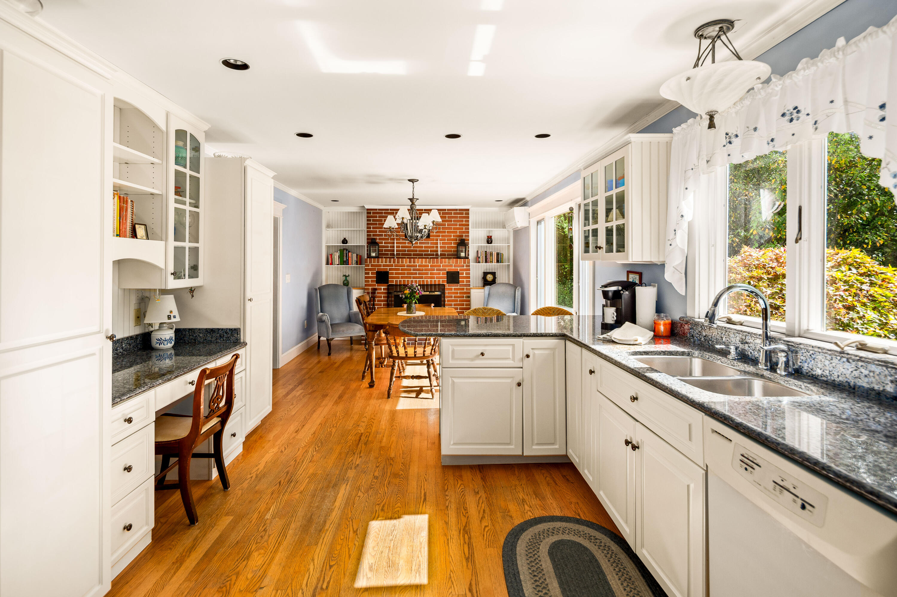 Bright kitchen with granite counters and a dining area beside a brick fireplace.