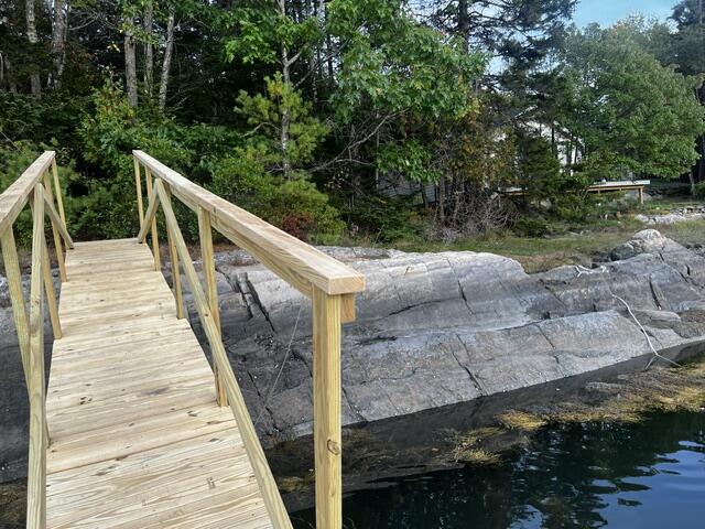 Wooden walkway beside a rocky, tree-lined shoreline and water.