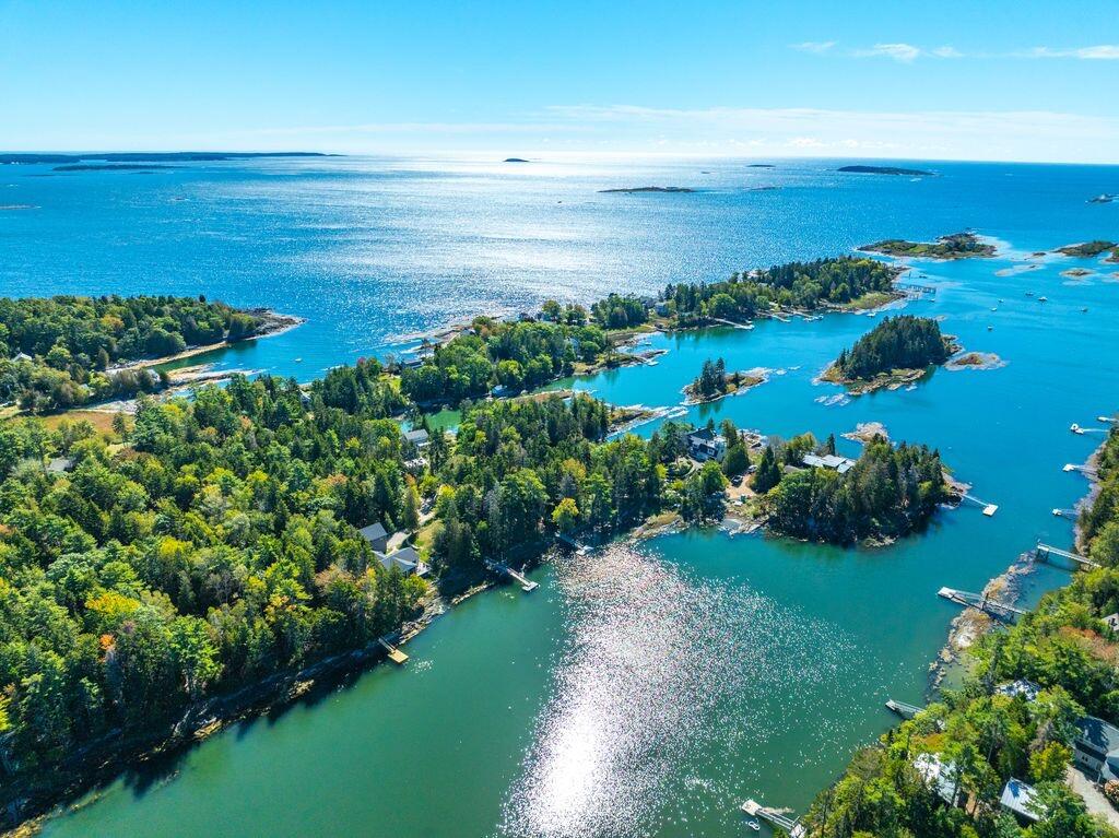 Aerial coastal view of wooded islands, shorefront homes, and blue water.