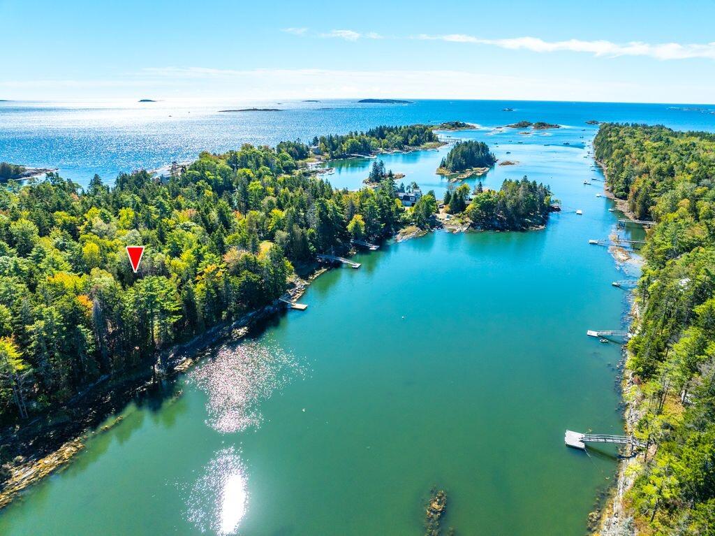 Aerial coastal inlet with wooded islands, docks, and a red marker at the shoreline.