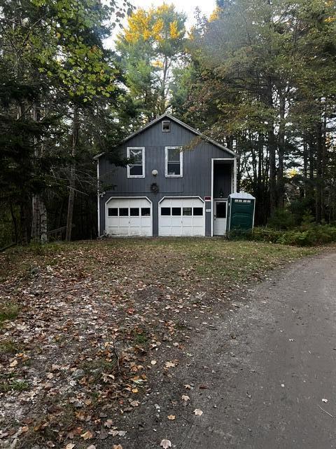 Dark gray detached garage with two white doors, surrounded by trees and autumn leaves.