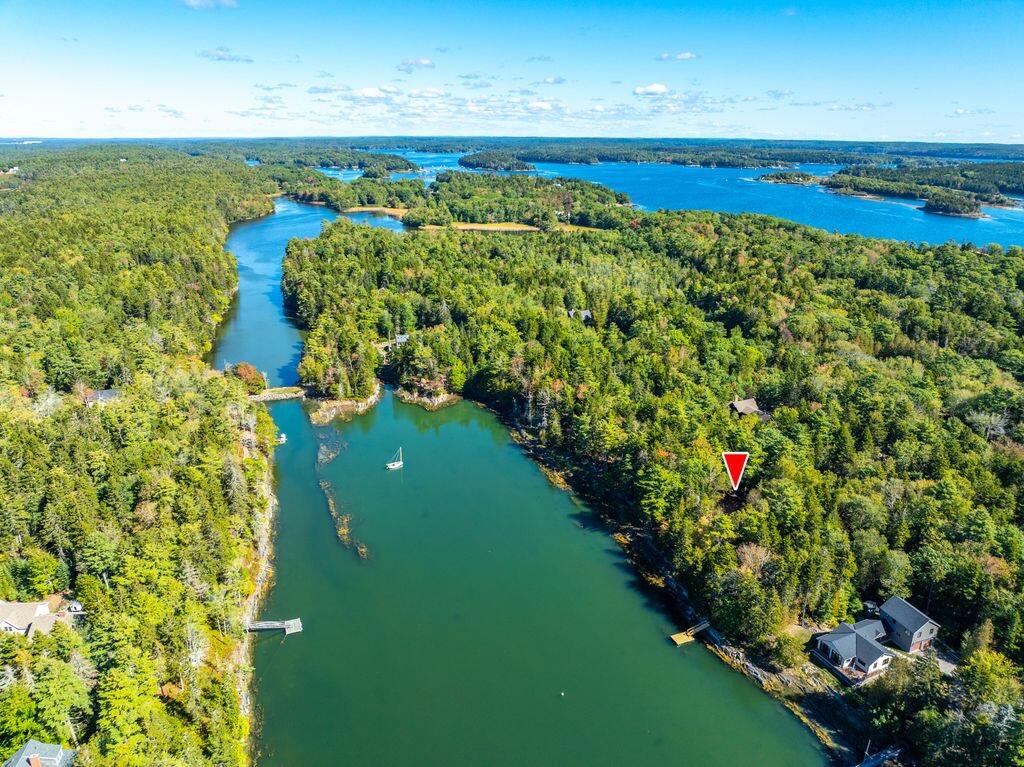 Aerial view of wooded waterfront property beside a cove, with docks and distant islands.