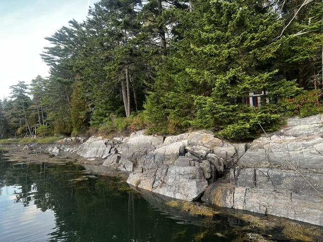 Rocky shoreline and calm water below a wooded property in Harpswell.