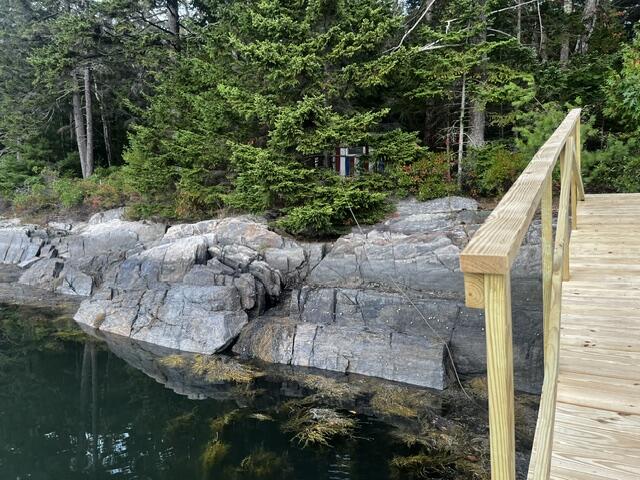 Rocky waterfront shoreline beside a wooden dock and dense trees.