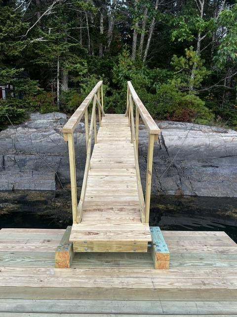 Wooden dock walkway crossing dark water to a rocky, tree-lined shore.