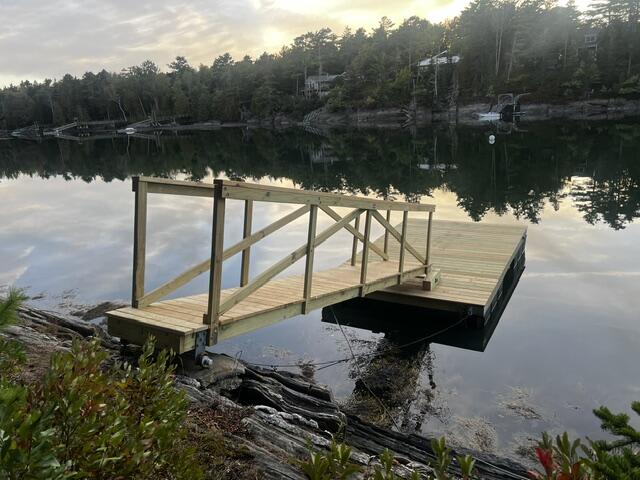 Wooden dock extends over calm water toward a wooded shoreline.