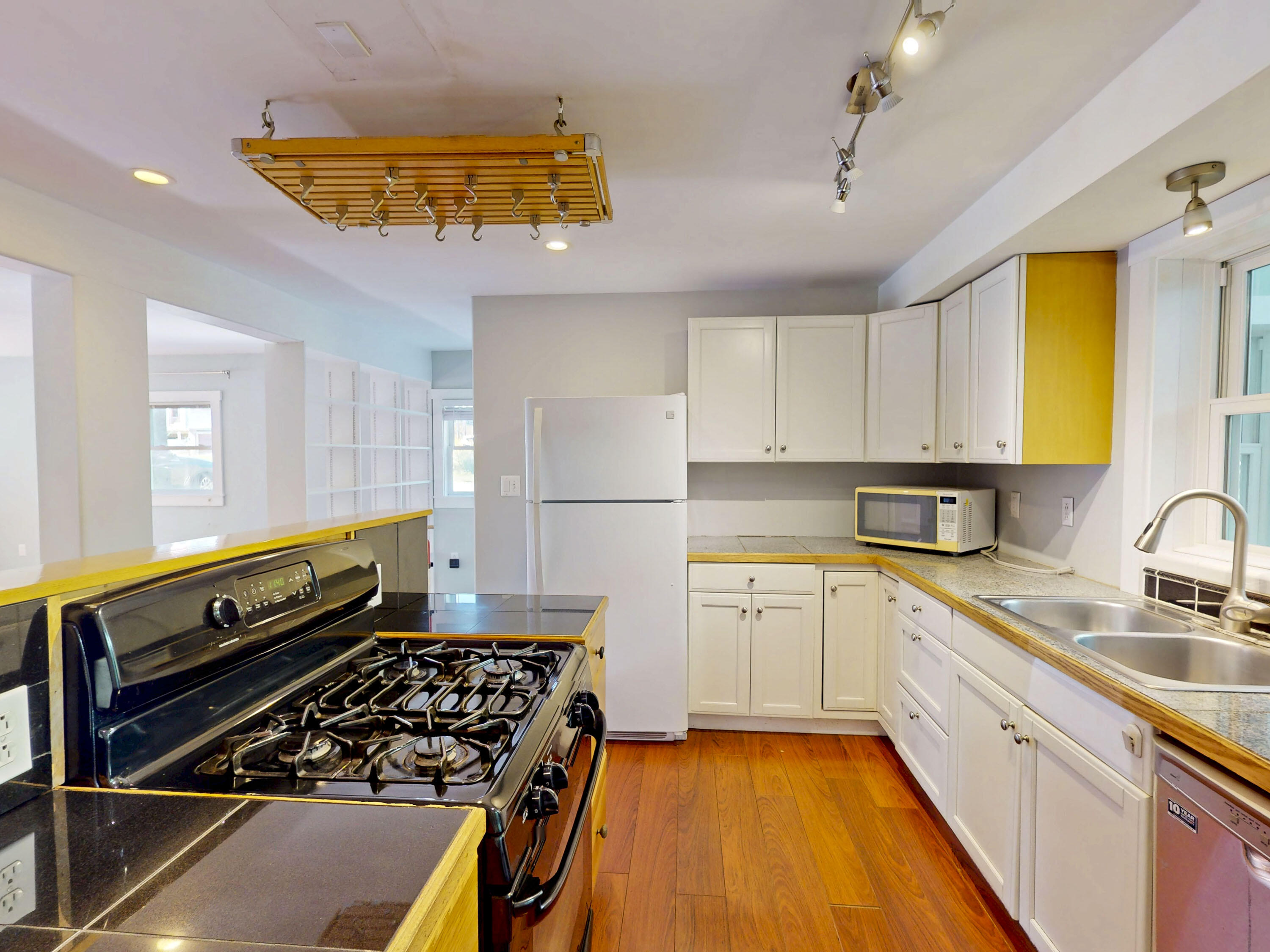 Kitchen with a black gas range, hanging pot rack, white cabinets, and hardwood floors.