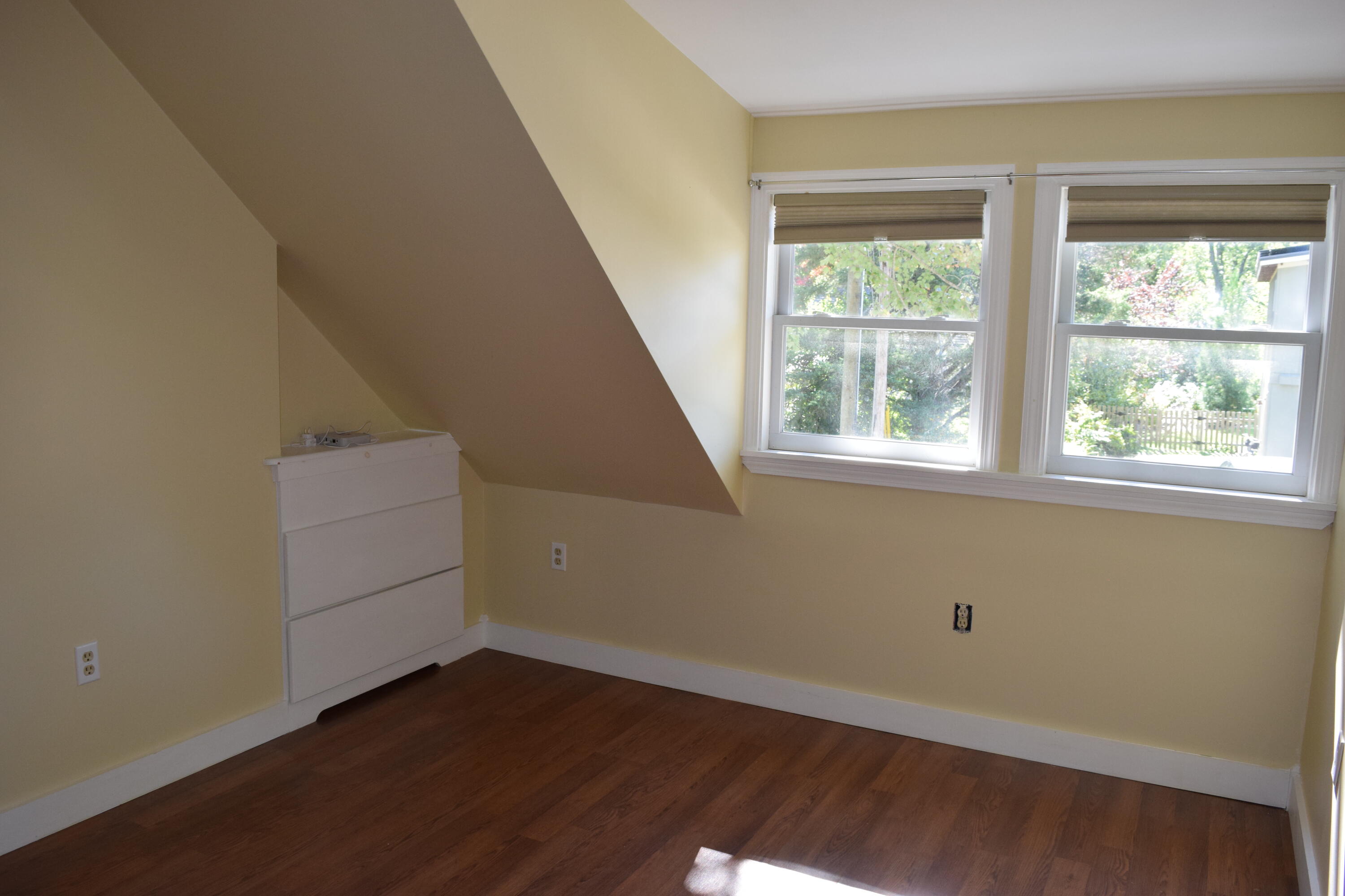 Empty room with a sloped ceiling, hardwood floor, and two windows.