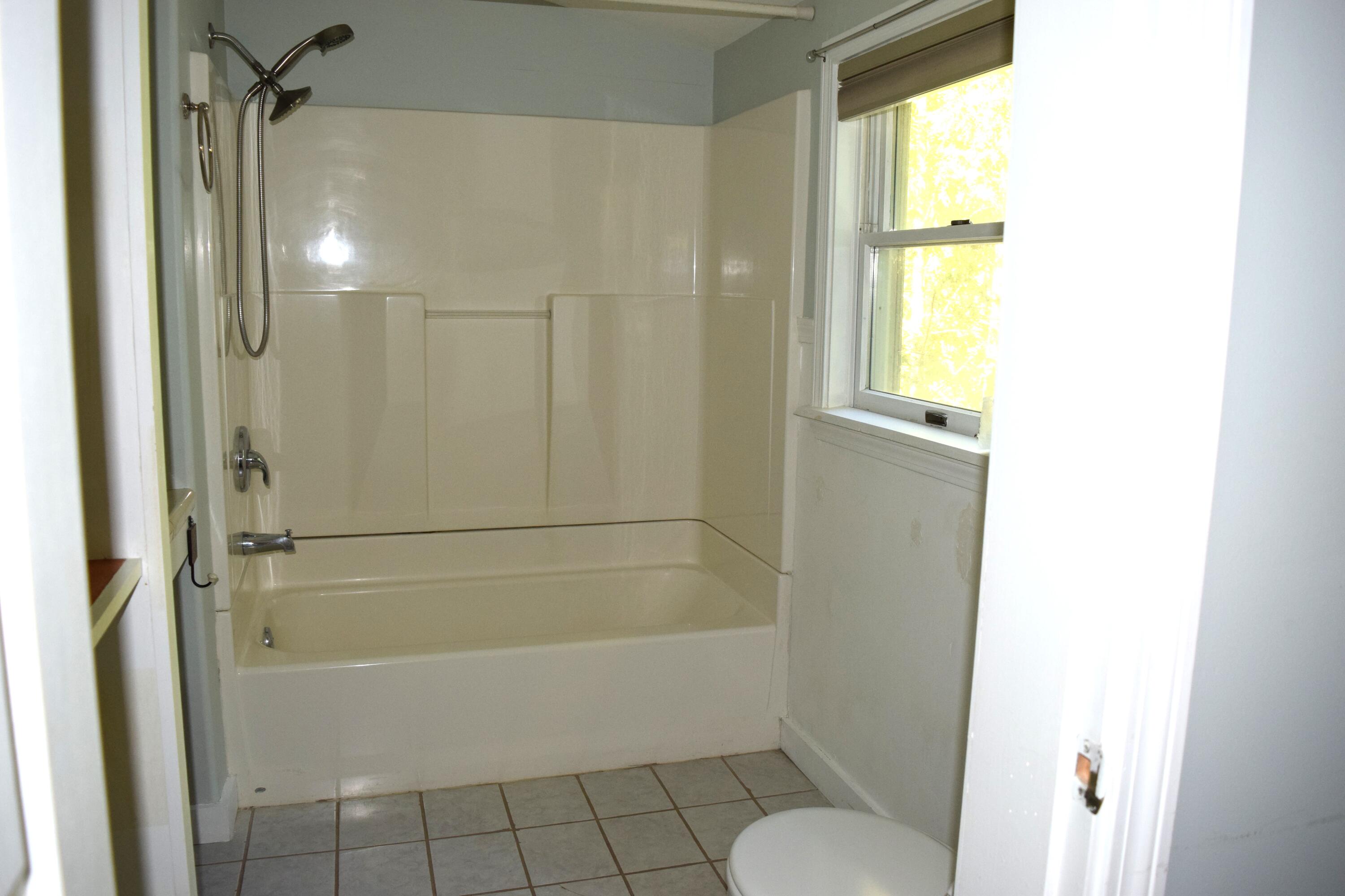 Bathroom with a bathtub and overhead shower beneath a window.