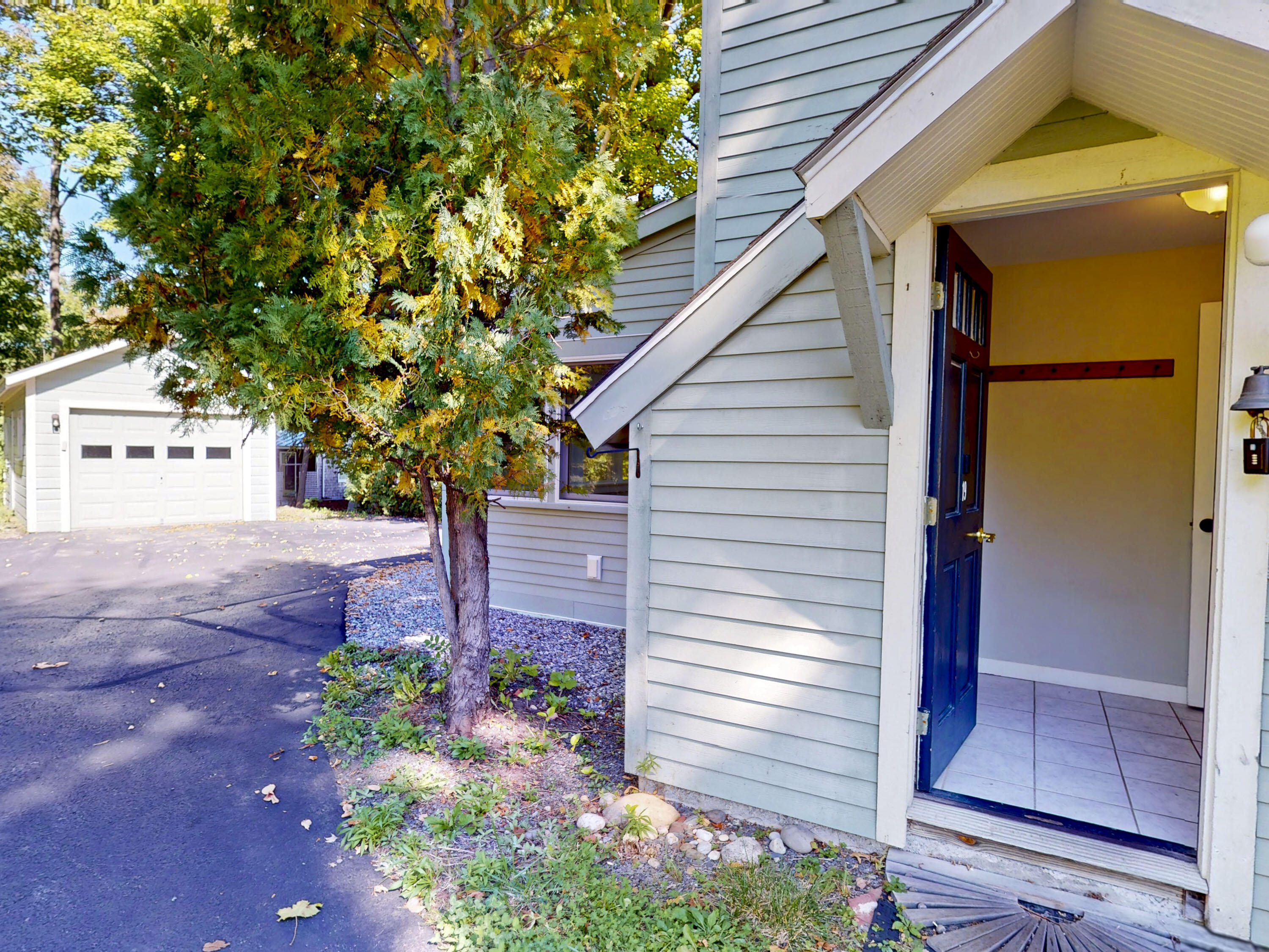 House entry with an open blue door, driveway, detached garage, and autumn trees.