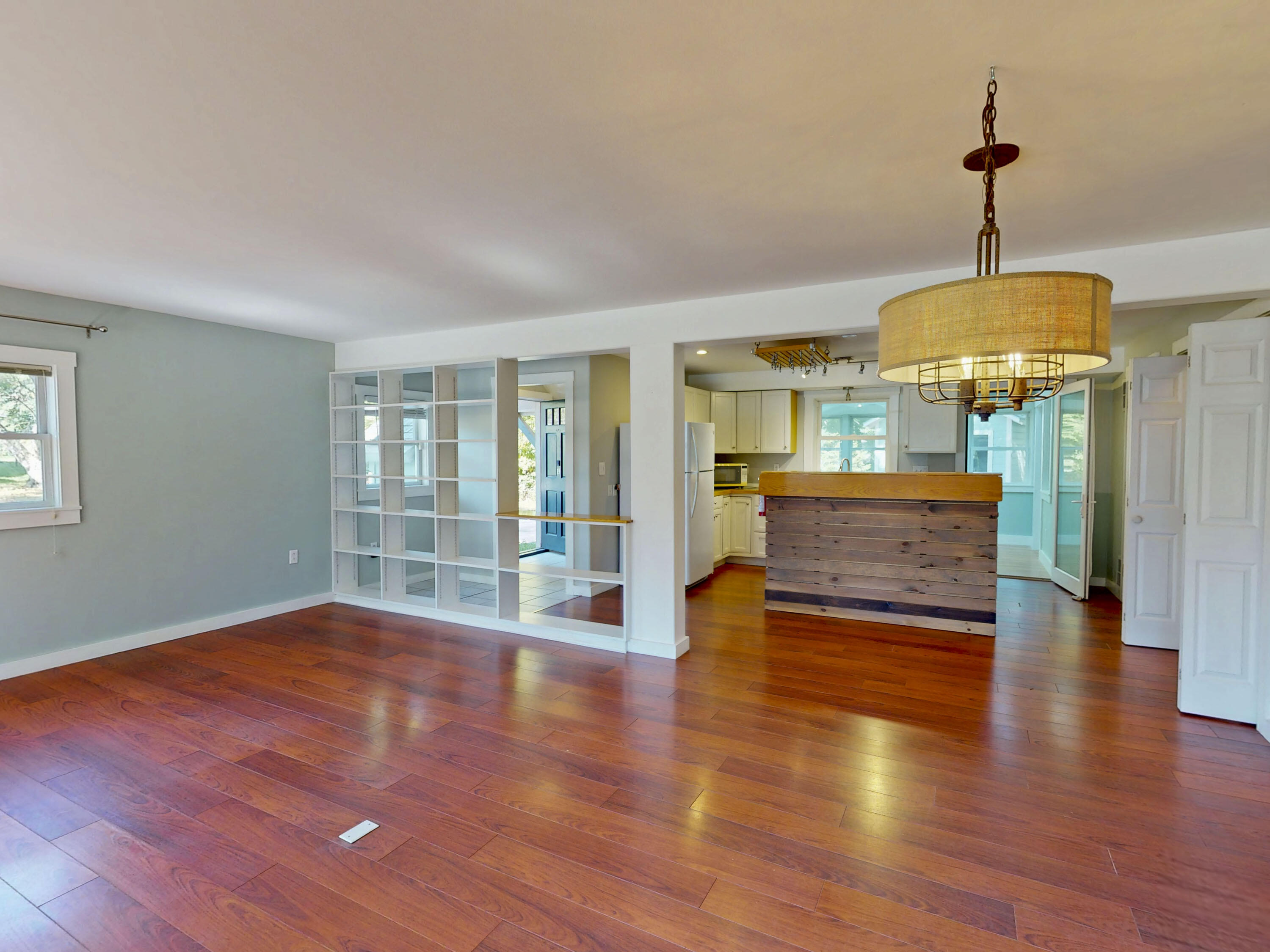 Open-plan living area and kitchen with hardwood floors, built-in shelving, and a wood-fronted island.