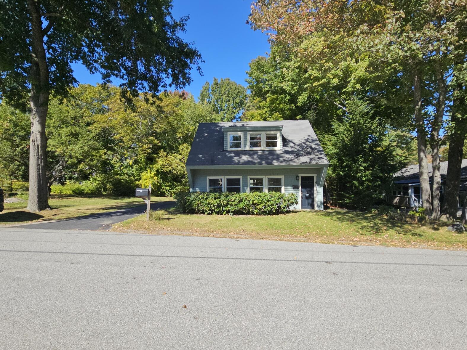 Blue two-story home with a prominent roof dormer, front hedge, and mature trees.