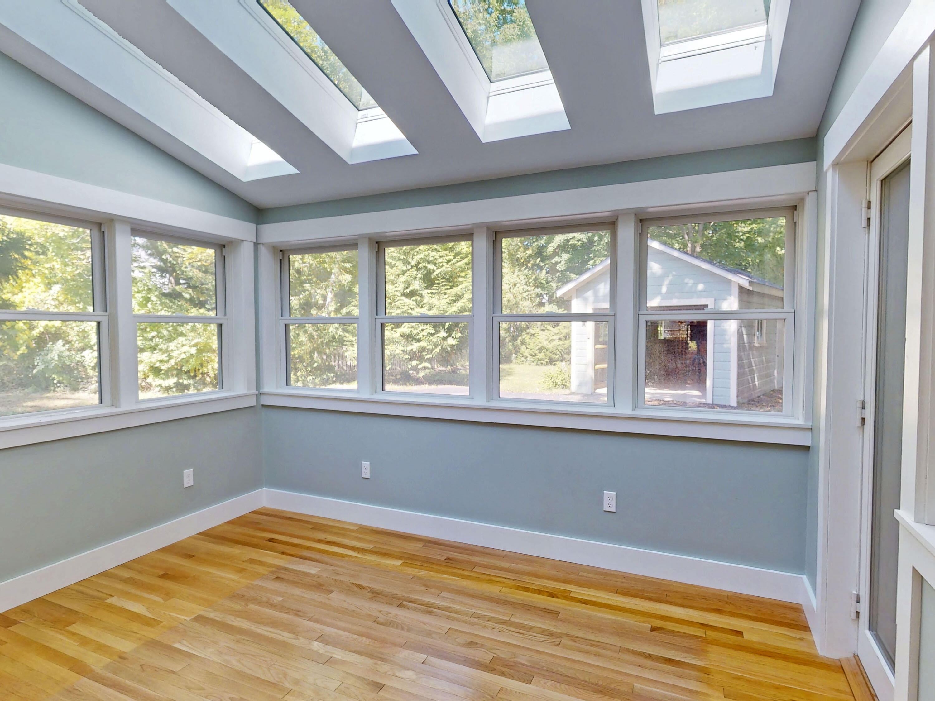Vacant sunroom with wraparound windows, multiple skylights, and hardwood floors.