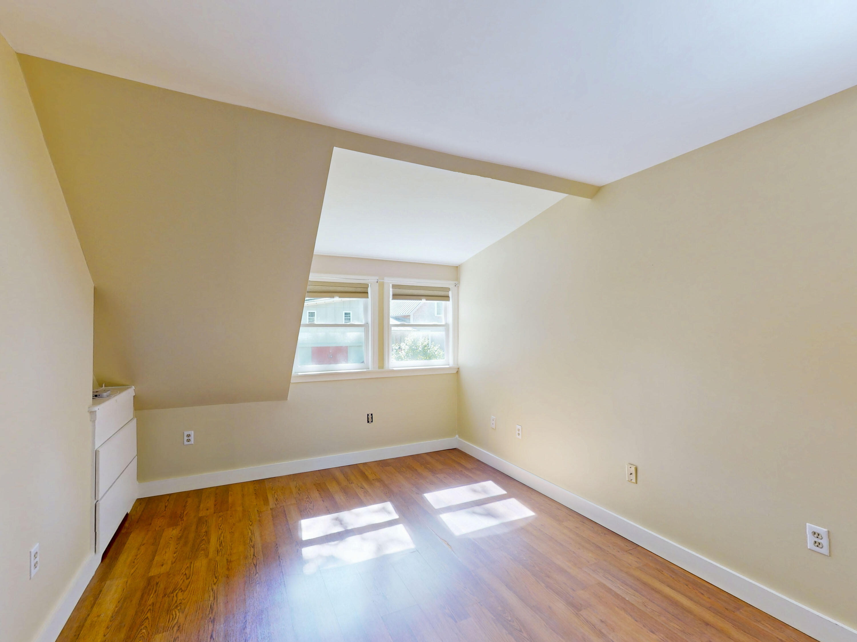 Vacant room with wood flooring, two windows, and a sloped ceiling.