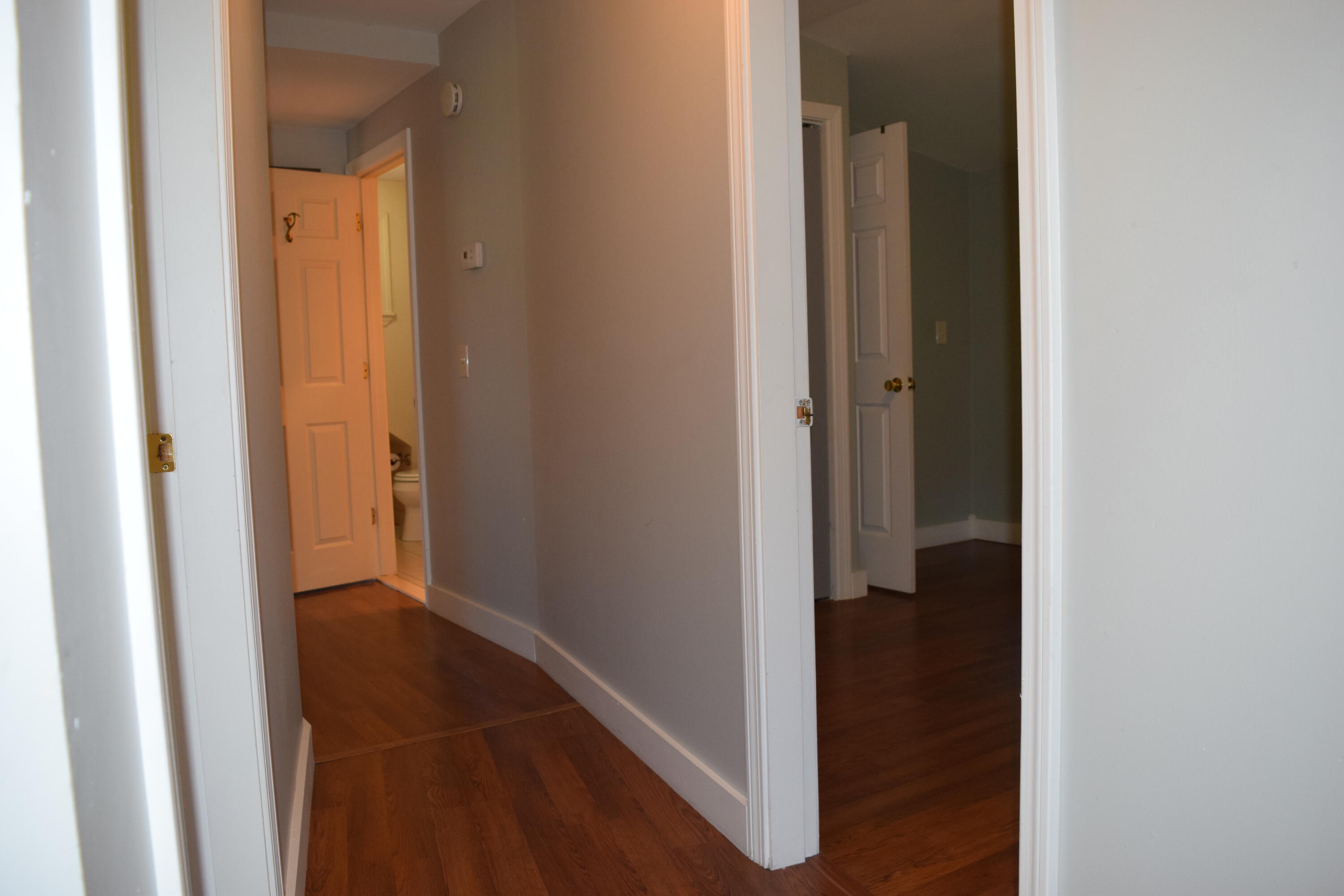 Empty hallway with dark hardwood floors and open doorways to a bathroom and adjoining room.