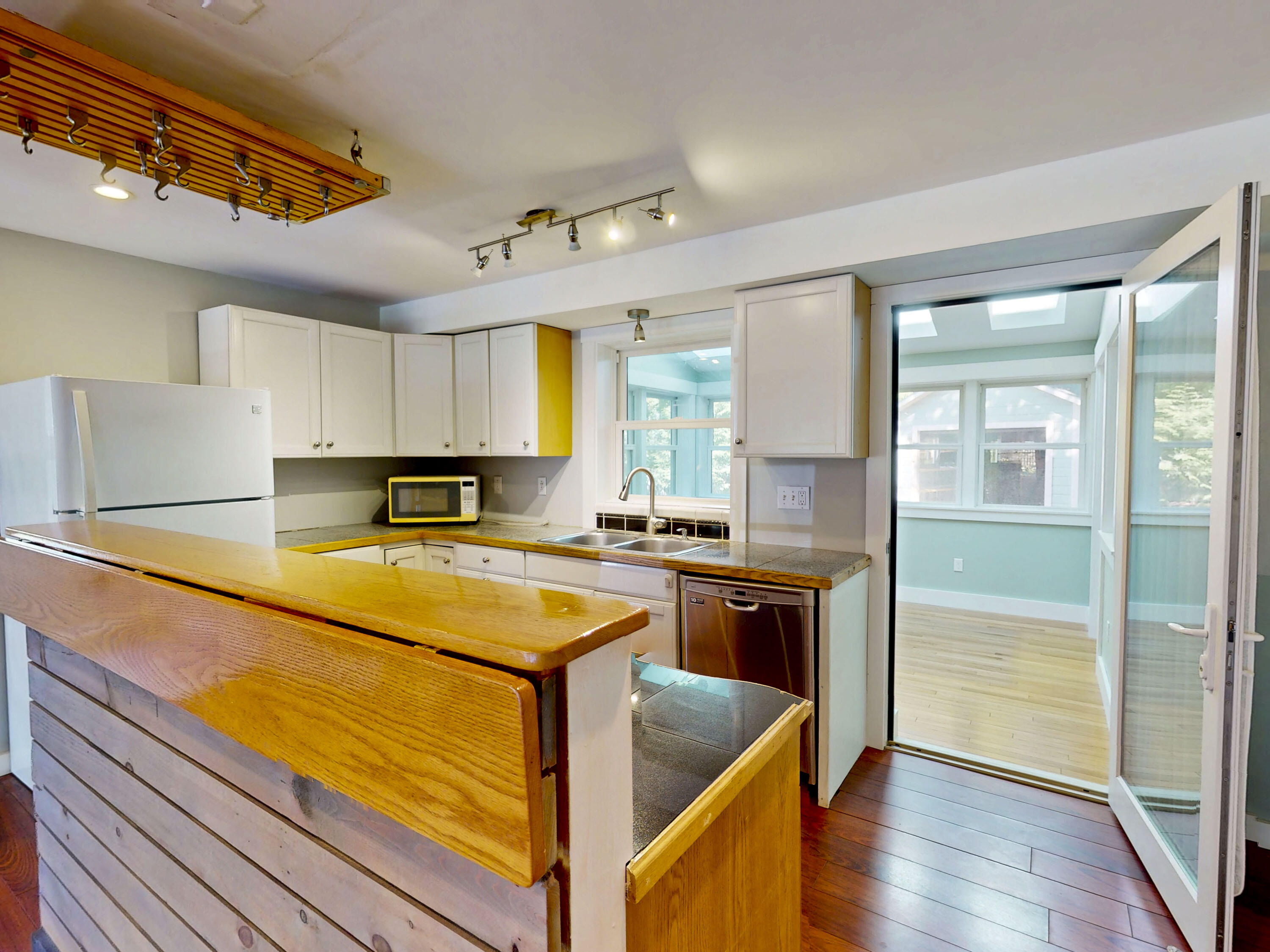 Kitchen with a broad wooden breakfast bar and open doors to a bright, skylit sunroom.
