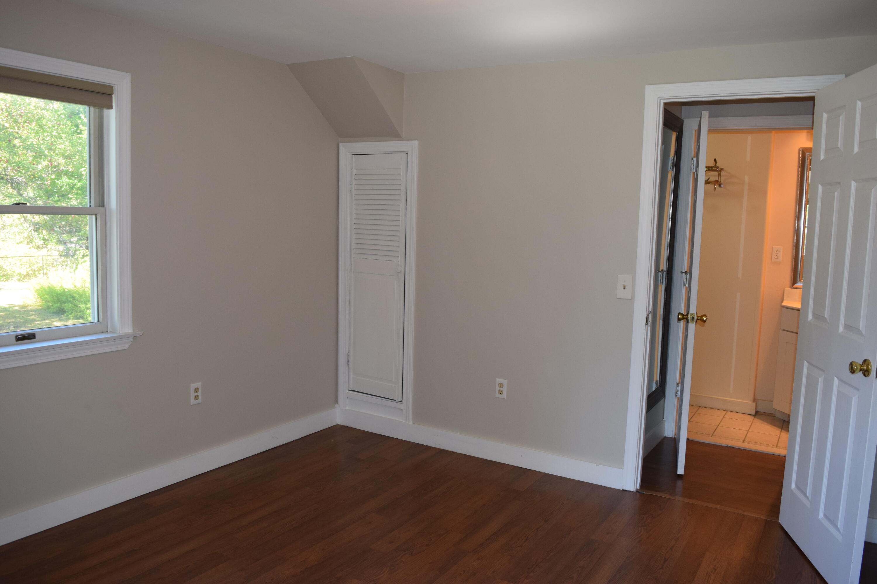Empty bedroom with hardwood floors, a window, and an adjoining bathroom.