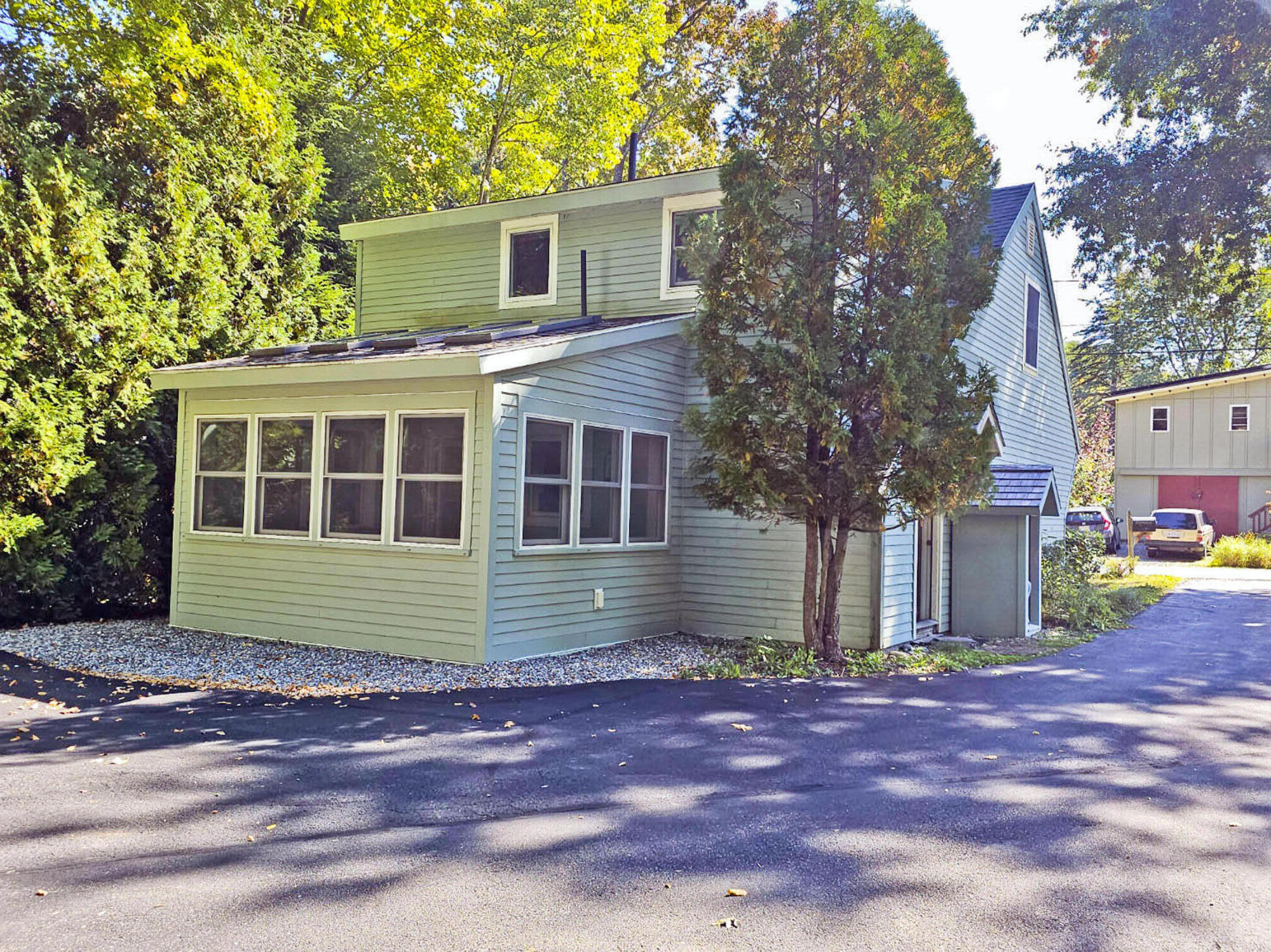 Blue-green two-story home with white-trimmed windows, an attached garage, and mature trees.