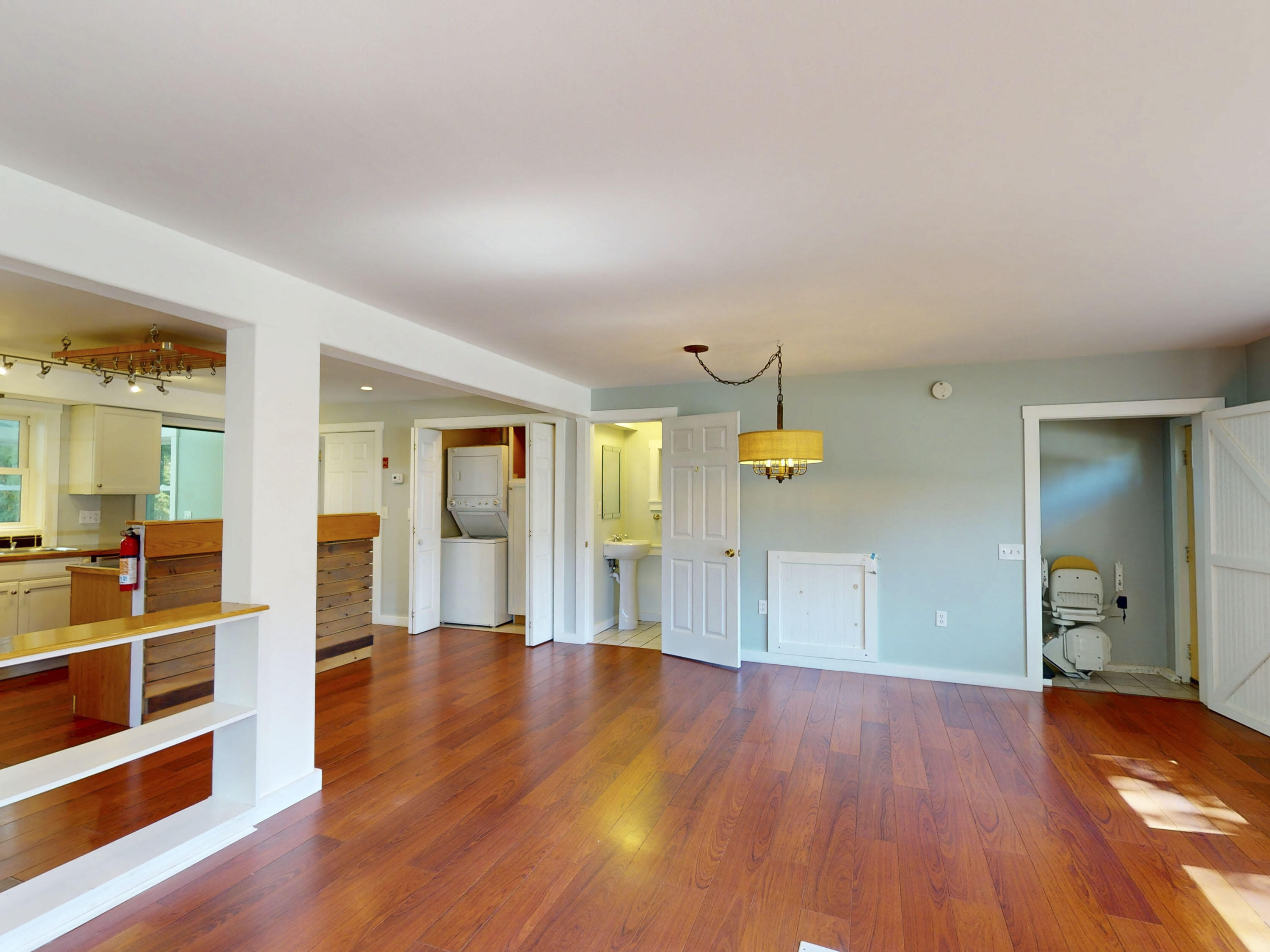Open living and dining area with reddish hardwood floors and views into the kitchen, laundry closet, and bathroom.