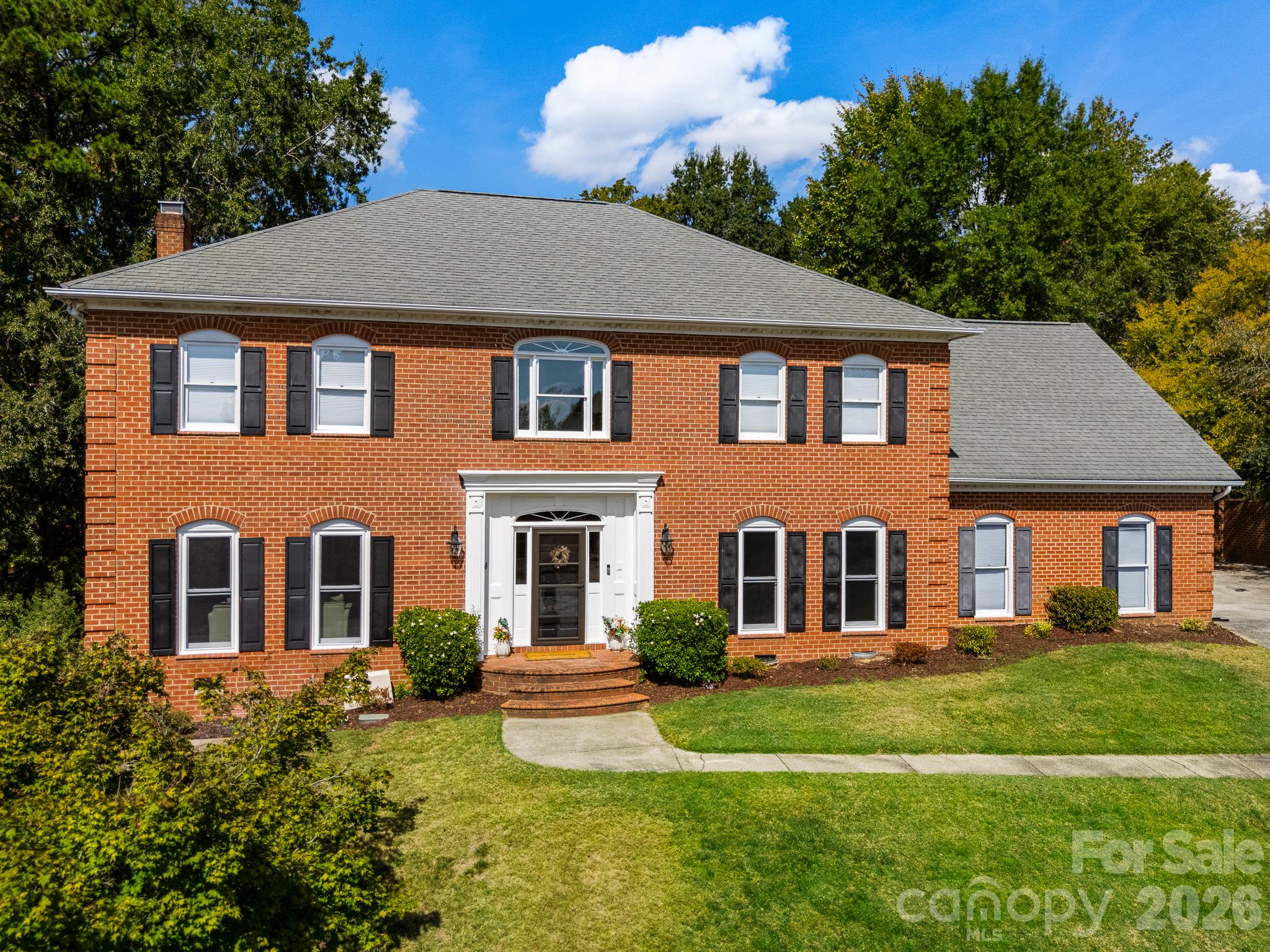 Two-story red brick house with black shutters, a white entry, and a green front lawn.