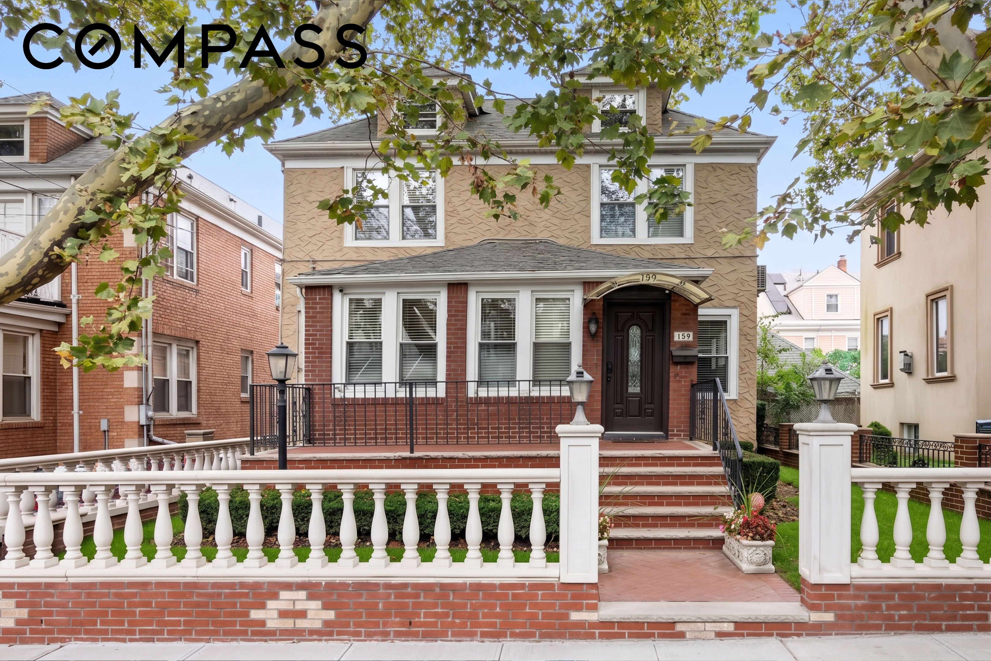 Two-story home with a brick entry porch and white balustrade beneath a leafy tree.